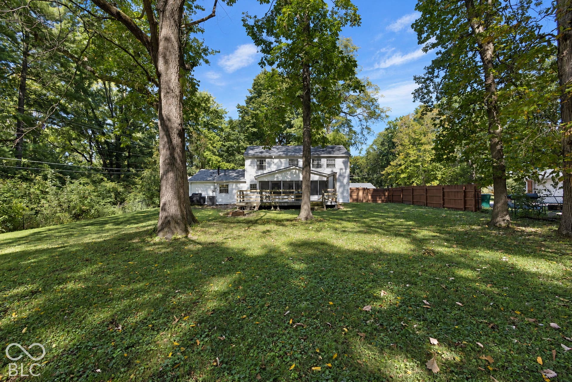 Expansive green lawn with mature trees, a two-story residence, screened-in porch, and a brown privacy fence