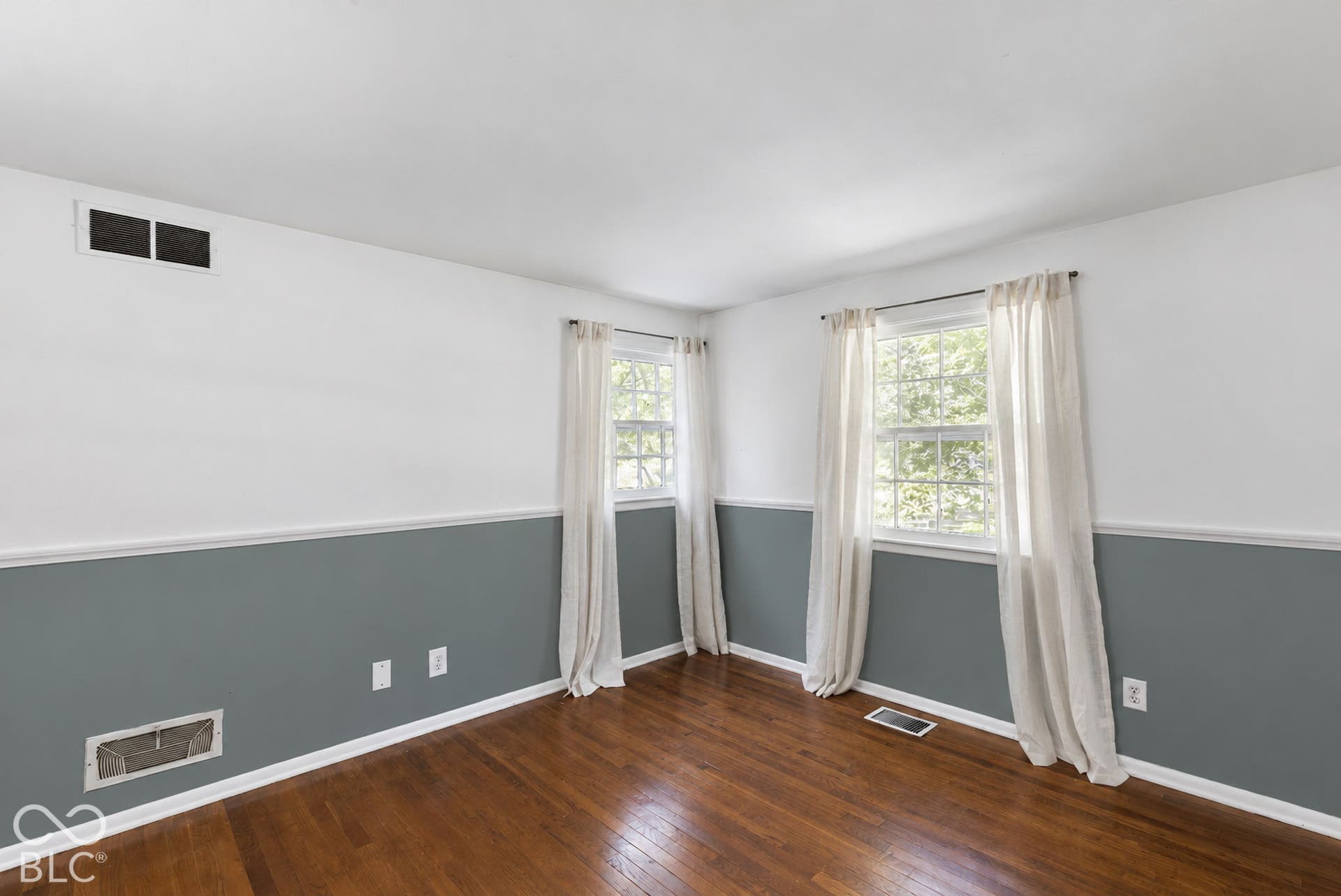 Wood-finish flooring with white trim, two windows, and two-tone painted walls