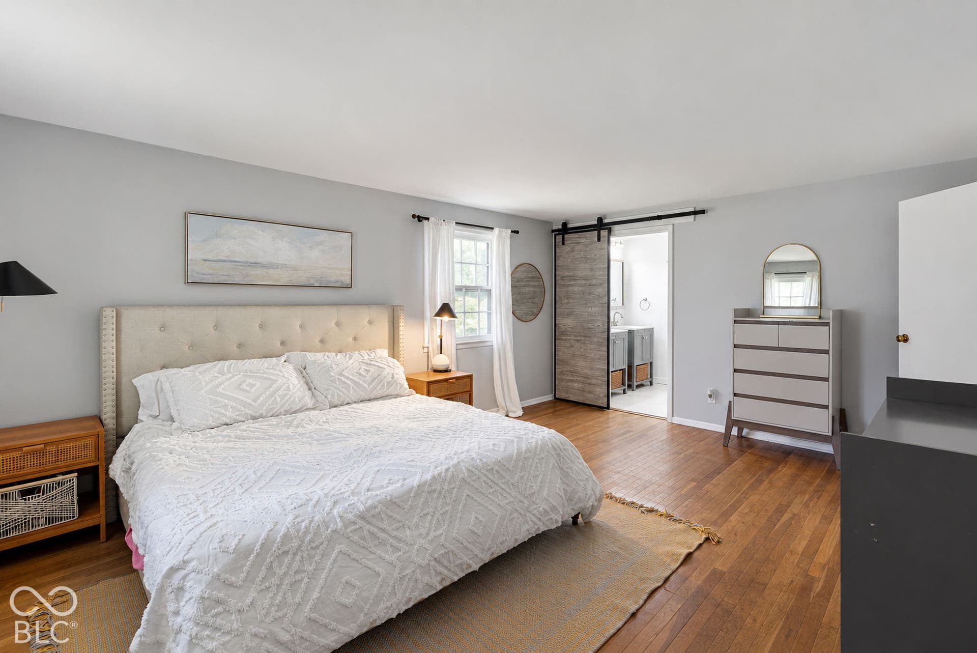Hardwood flooring, light gray wall color, barn door entry, natural light from window, tufted headboard