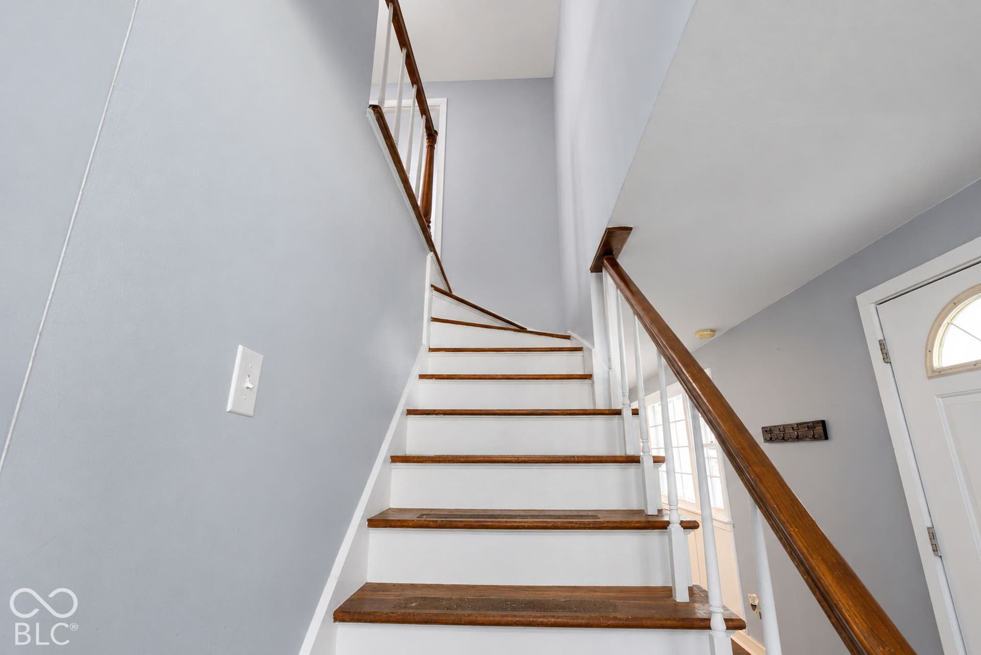 Stairway featuring wood-finish treads and risers, white balusters, and a wood-finish handrail