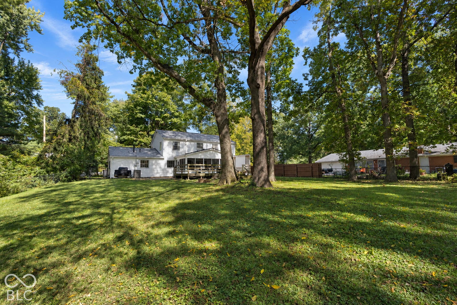 Expansive green lawn with mature trees and a screened-in porch with wood deck
