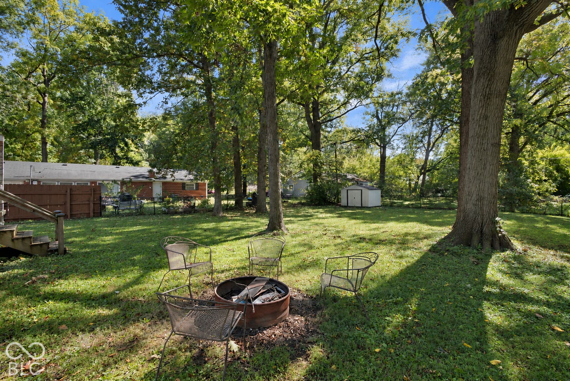 Expansive grassy yard with mature trees, a storage shed, and a privacy fence