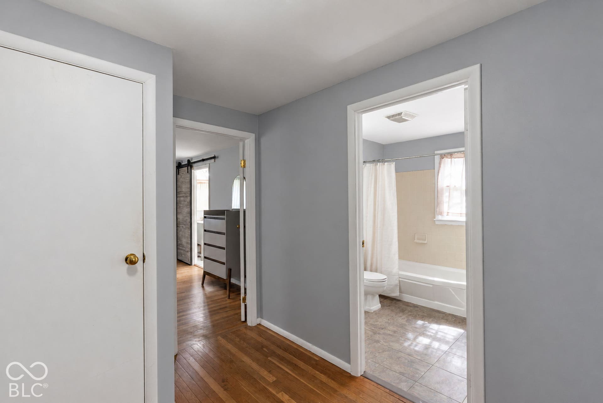Hardwood flooring, painted walls, white door, doorway, bathroom with white tub