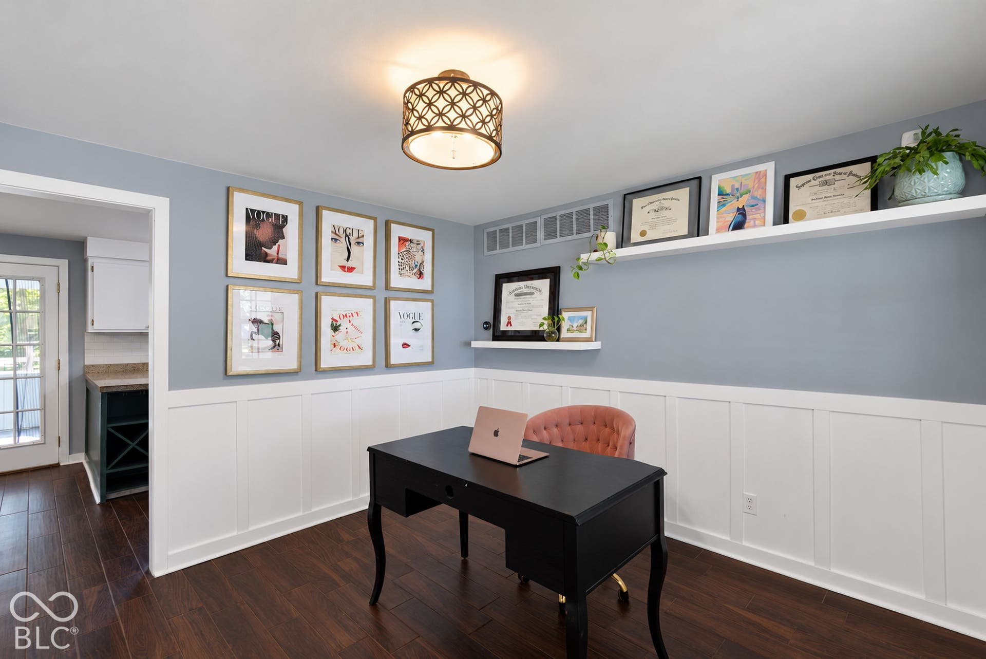 Hardwood-style flooring, white wainscoting, light blue wall paint, two wall-mounted shelves, and a decorative ceiling light fixture