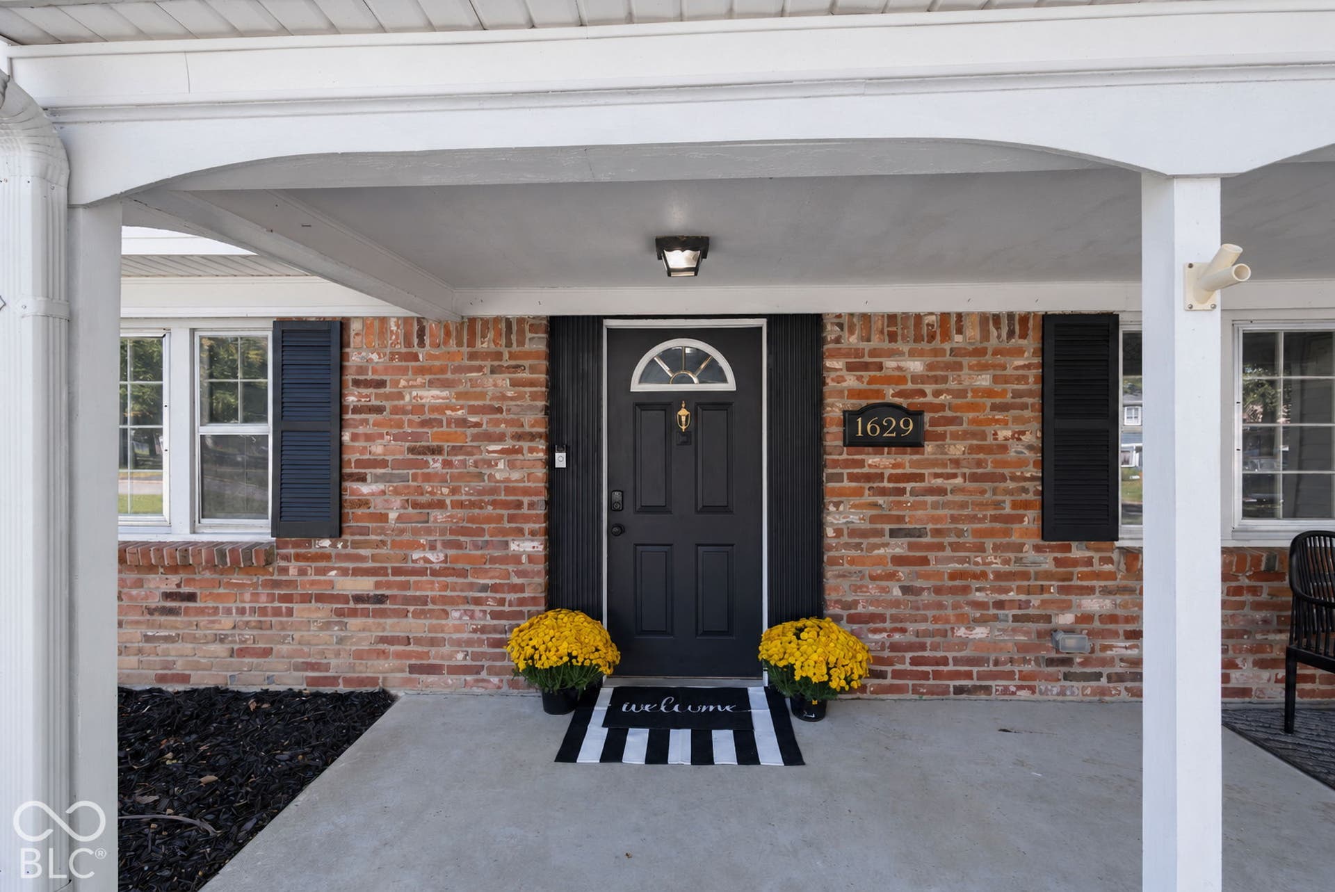 Welcoming and cozy exterior with white porch columns, covered entryway, black front door with decorative window, and dark shutters