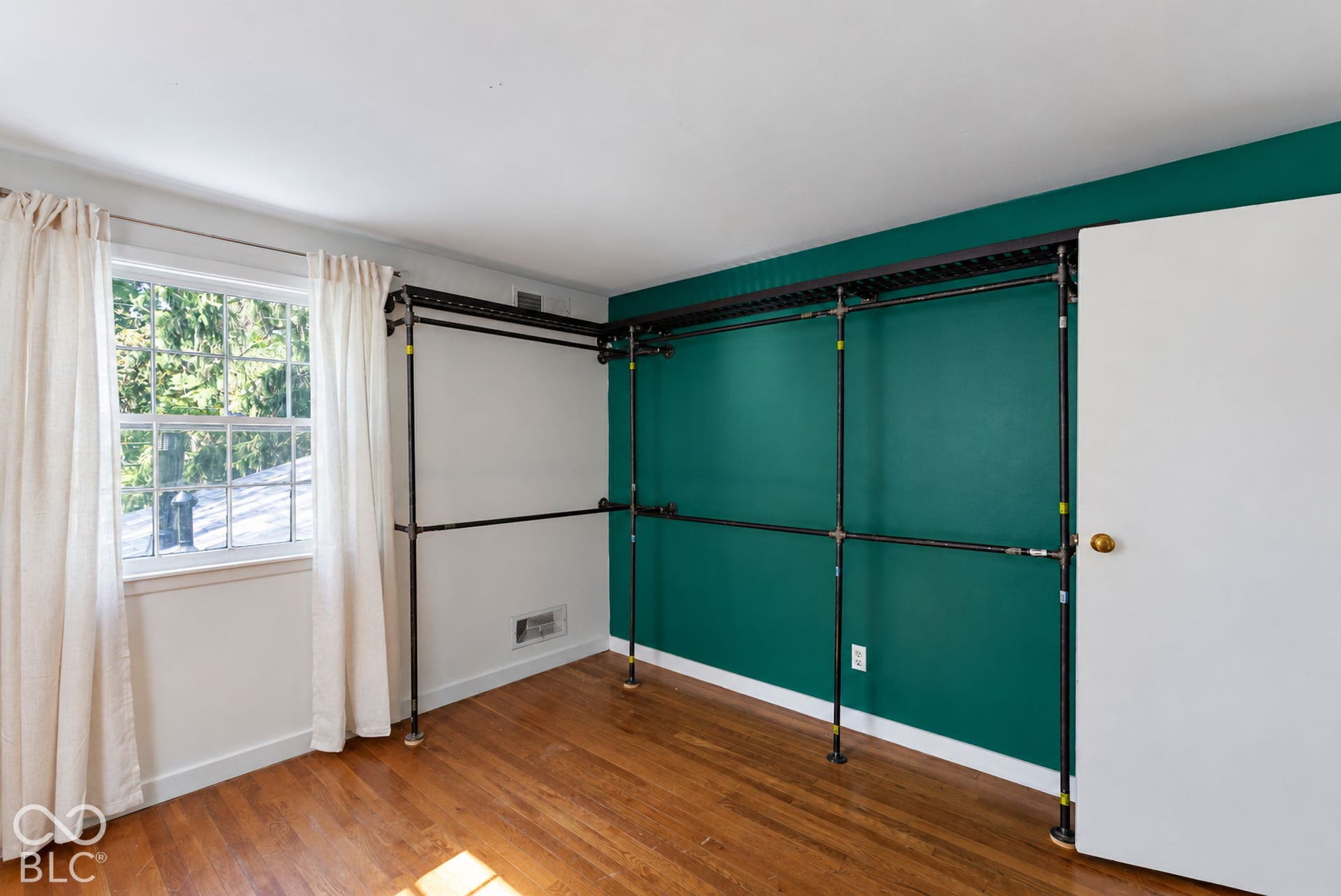 Hardwood flooring, multi-pane window, bright white trim, custom wall-mounted shelving system, and a solid core door