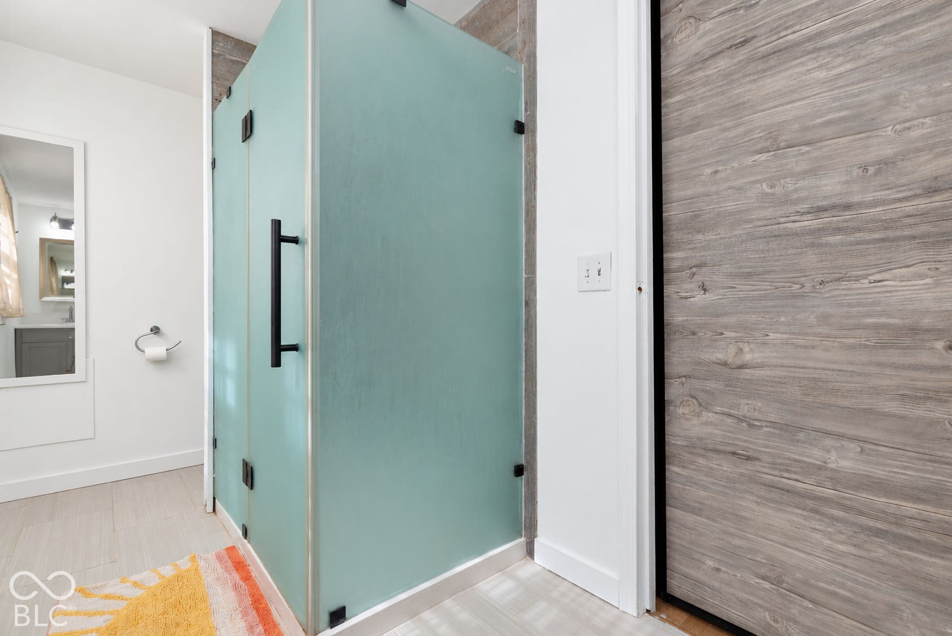 Frosted glass shower enclosure with matte black hardware, wood-look wall paneling, and light-toned flooring