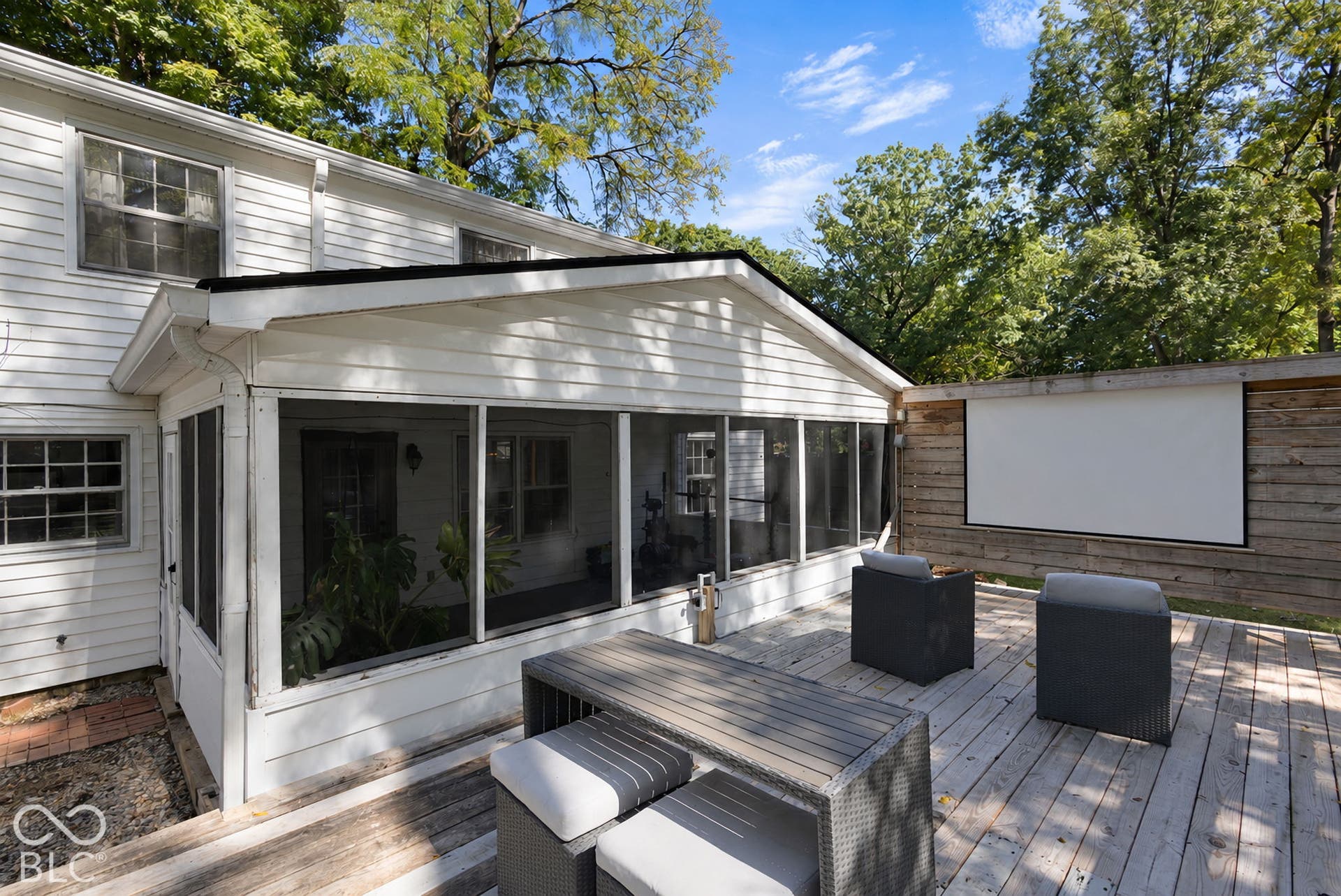 Expansive wood deck with a built-in outdoor projection screen, complemented by a screened-in porch with white siding