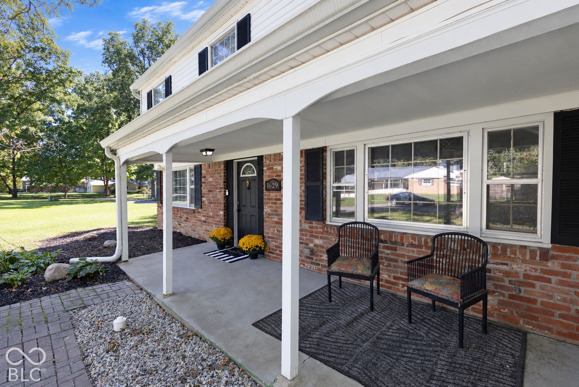 Brick facade with white siding, covered front porch, concrete porch floor, and black shutters