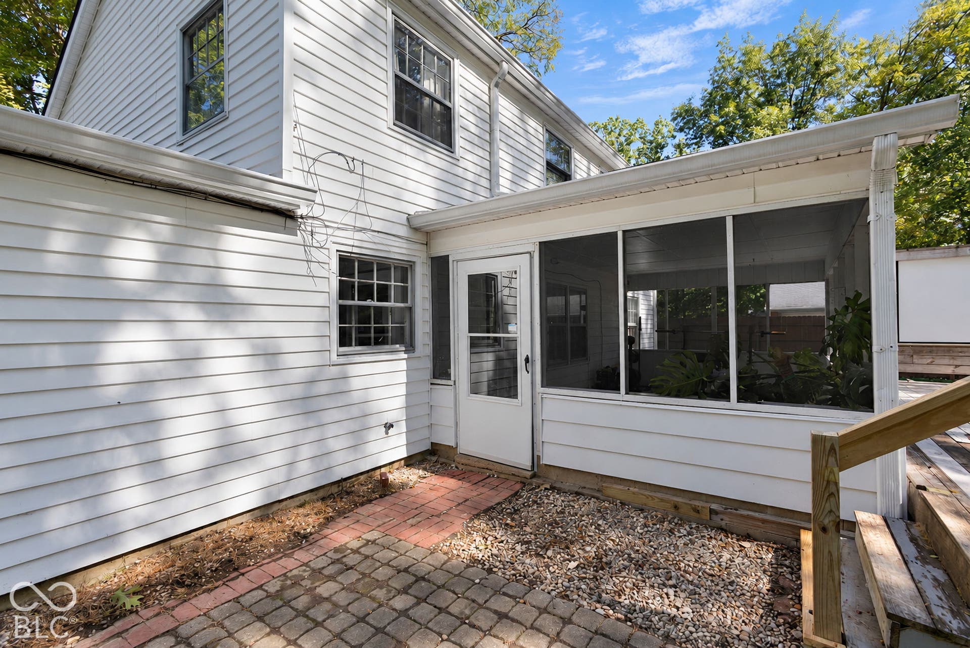Screened porch with white siding, leading to a paver patio area will allow you to continue to enjoy this lovely and peaceful backyard all year round and could be heated in the future to help in the colder months