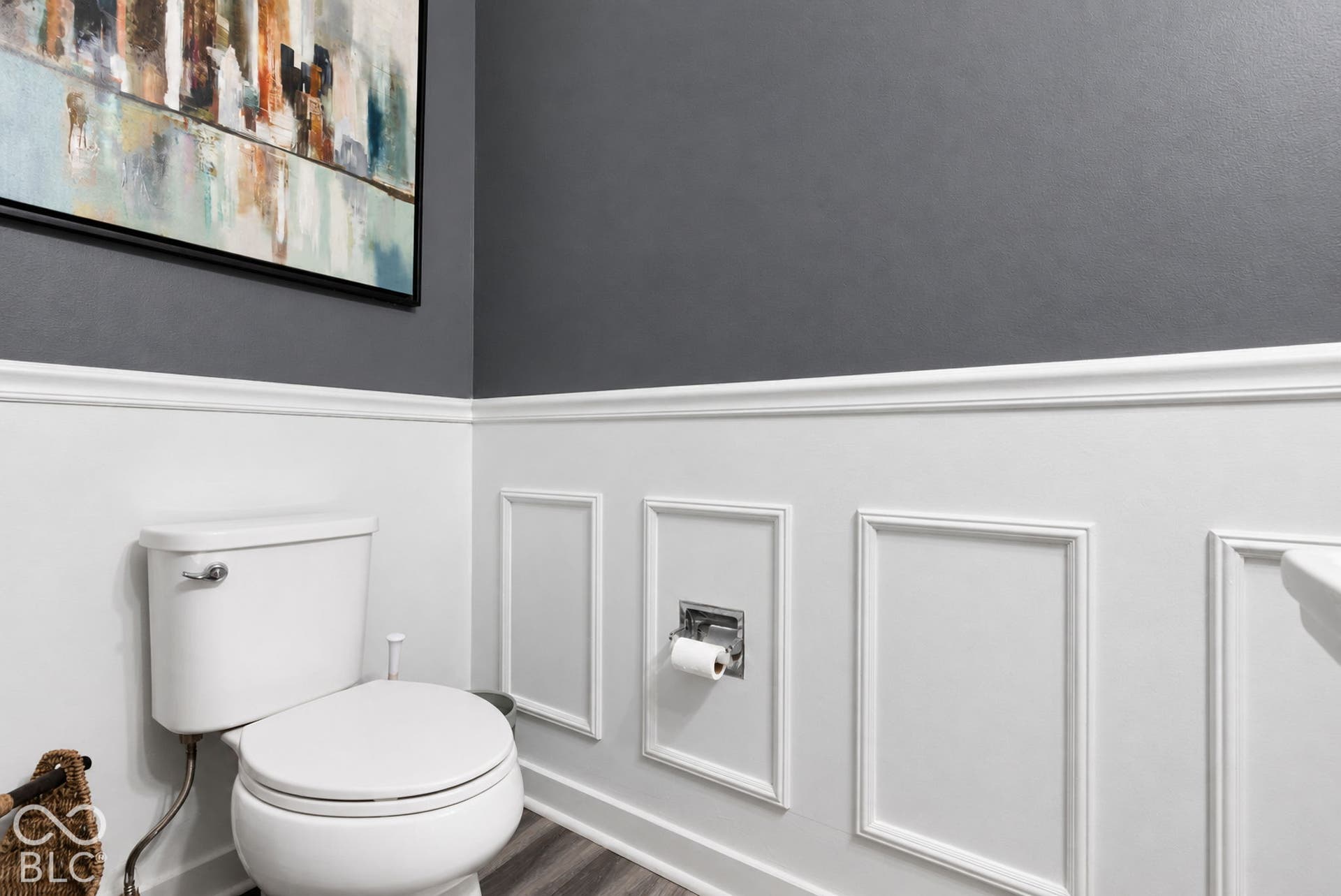 White wainscoting with decorative trim, dark gray painted walls, wood-finish flooring, and a white toilet
