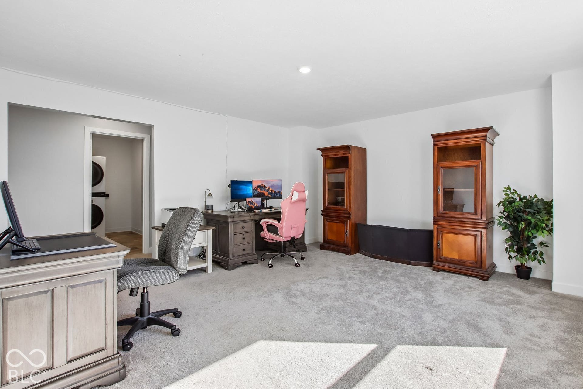 Carpeted room with white walls, recessed ceiling lighting, and a doorway revealing a stacked washer and dryer