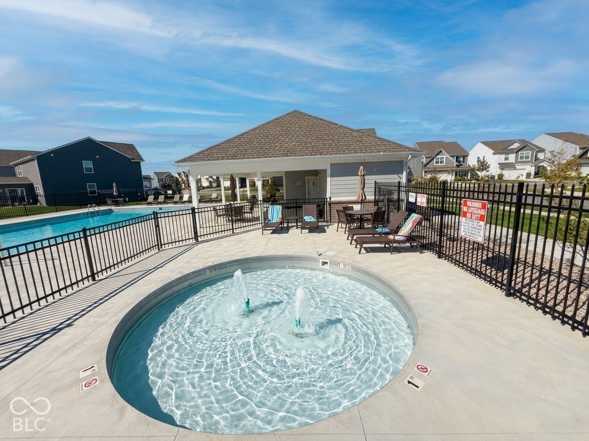 Outdoor pool area featuring a circular wading pool with fountains, a rectangular swimming pool, and a shaded pavilion