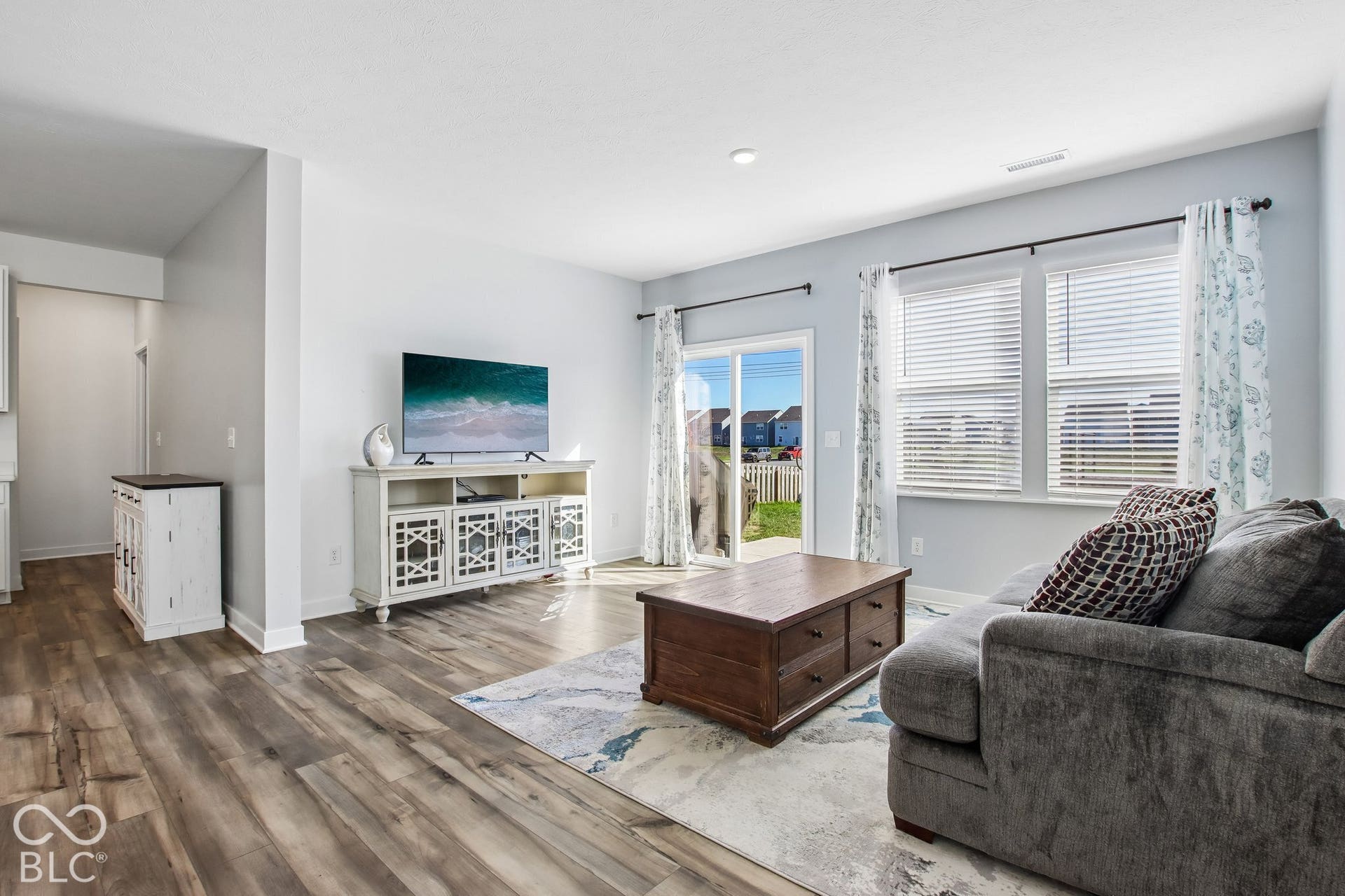Wood-finish flooring throughout, multiple windows with blinds, and a sliding glass door providing exterior access
