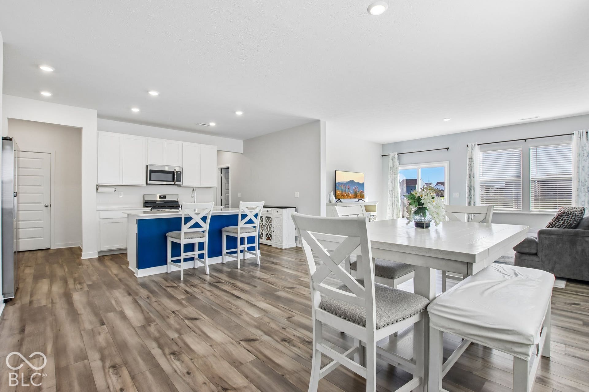 Open-concept living area featuring wood-finish flooring, a kitchen with white cabinetry, a blue kitchen island, and stainless steel appliances