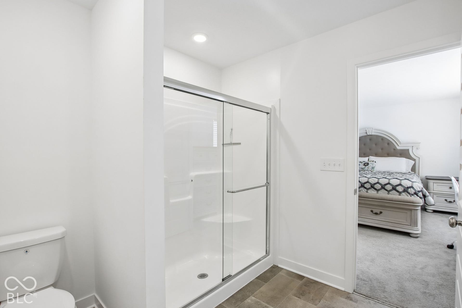 White toilet with a glass-enclosed shower featuring a built-in shelf and bench