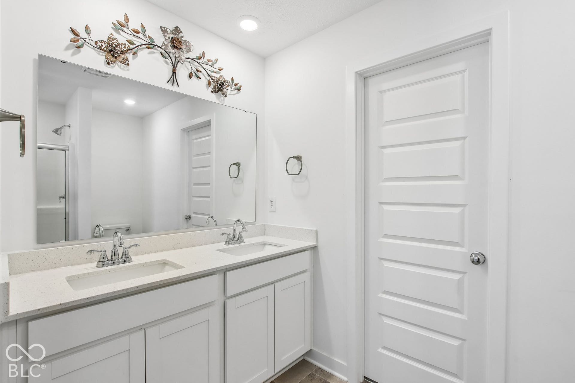 Dual undermount sinks set in a light-toned countertop, white cabinetry, large vanity mirror, and recessed lighting