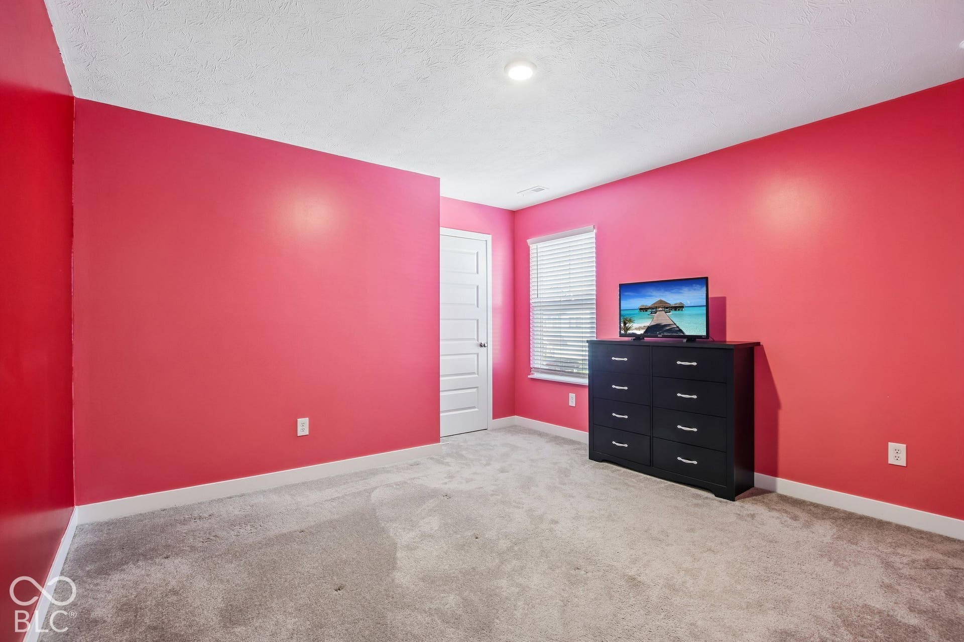 Recessed ceiling lighting illuminates a room featuring a five-panel interior door, a window with horizontal blinds, and carpet flooring