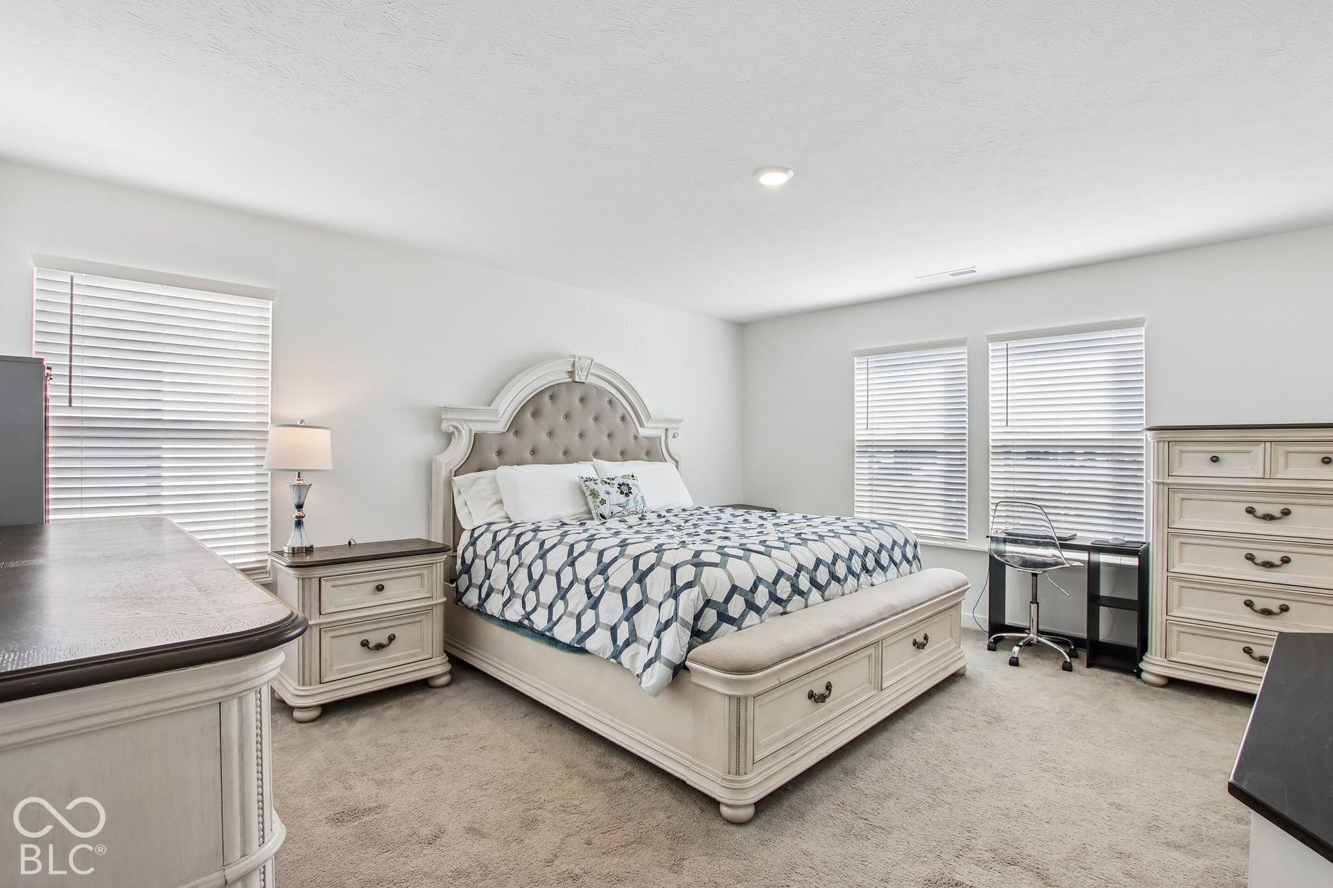 Plush carpet flooring complements bright white walls and multiple windows with horizontal blinds