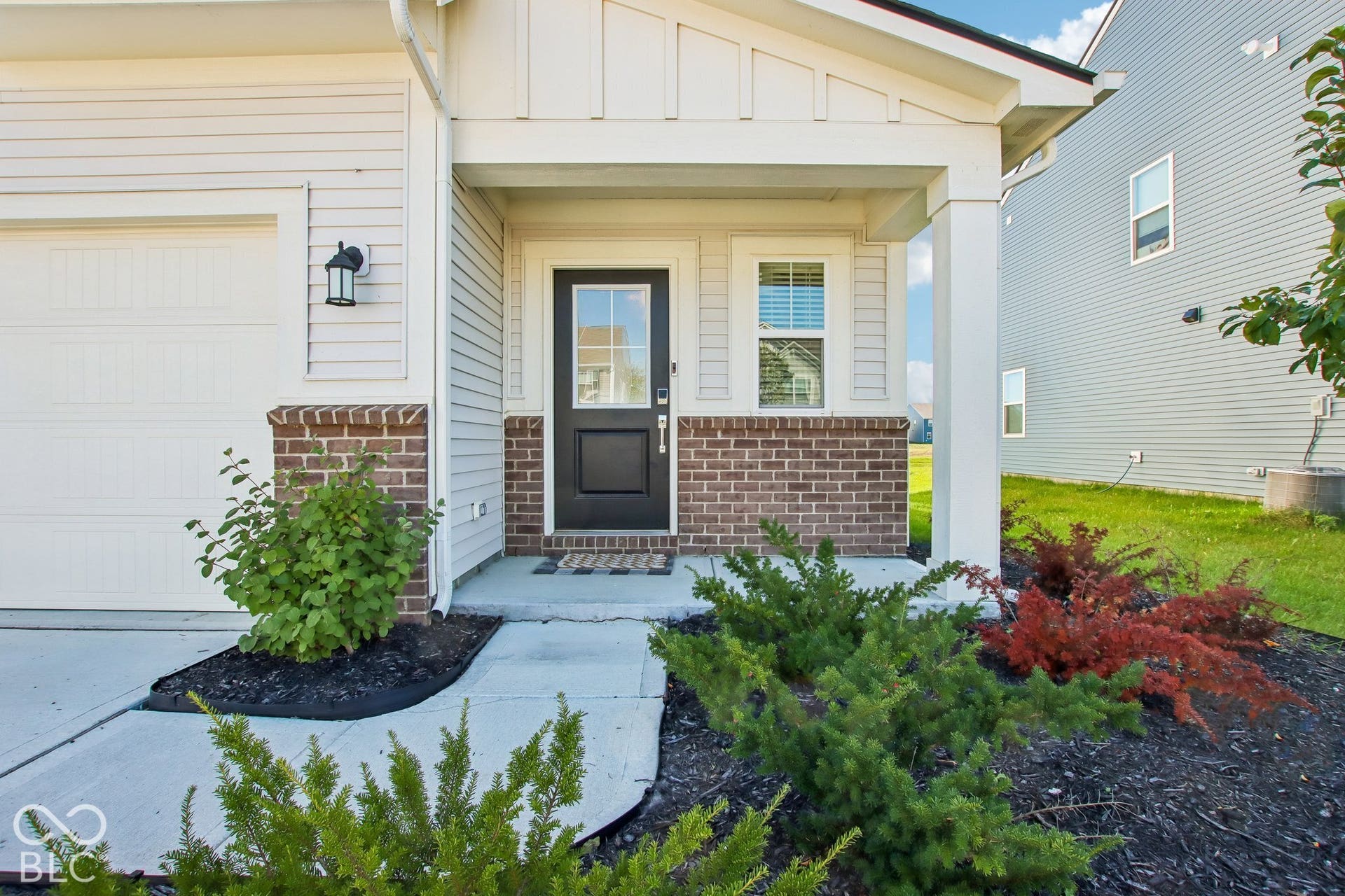 Covered entry with a solid black door, brick veneer siding, and a single-car garage