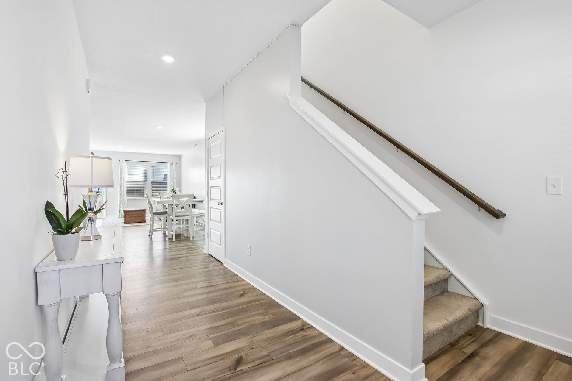 Wood-finish flooring, white trim, recessed lighting, white panel door, and carpeted stairs with a dark wood handrail