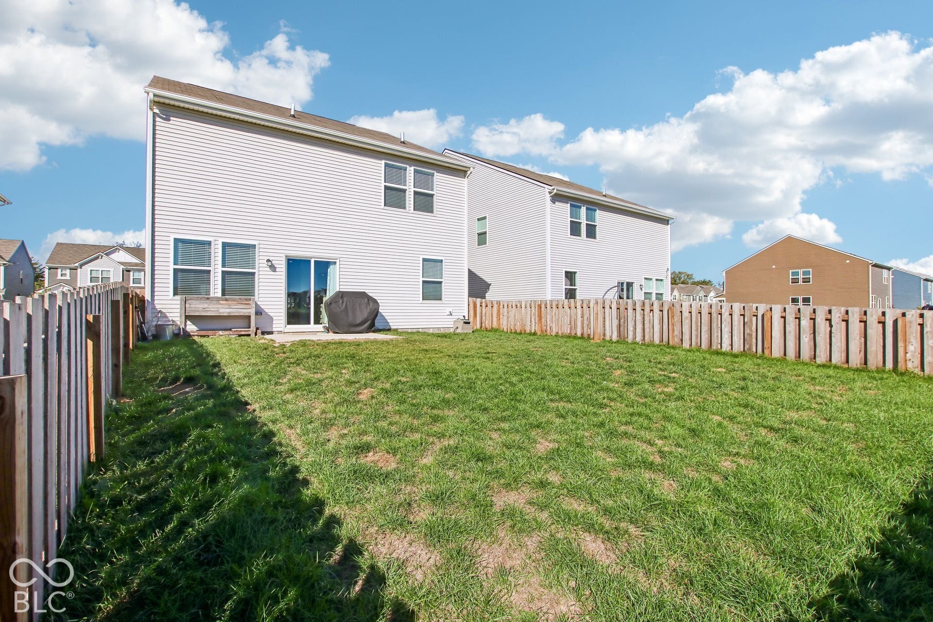 Expansive backyard featuring a manicured lawn, a wooden privacy fence, and a patio area with a sliding glass door entry