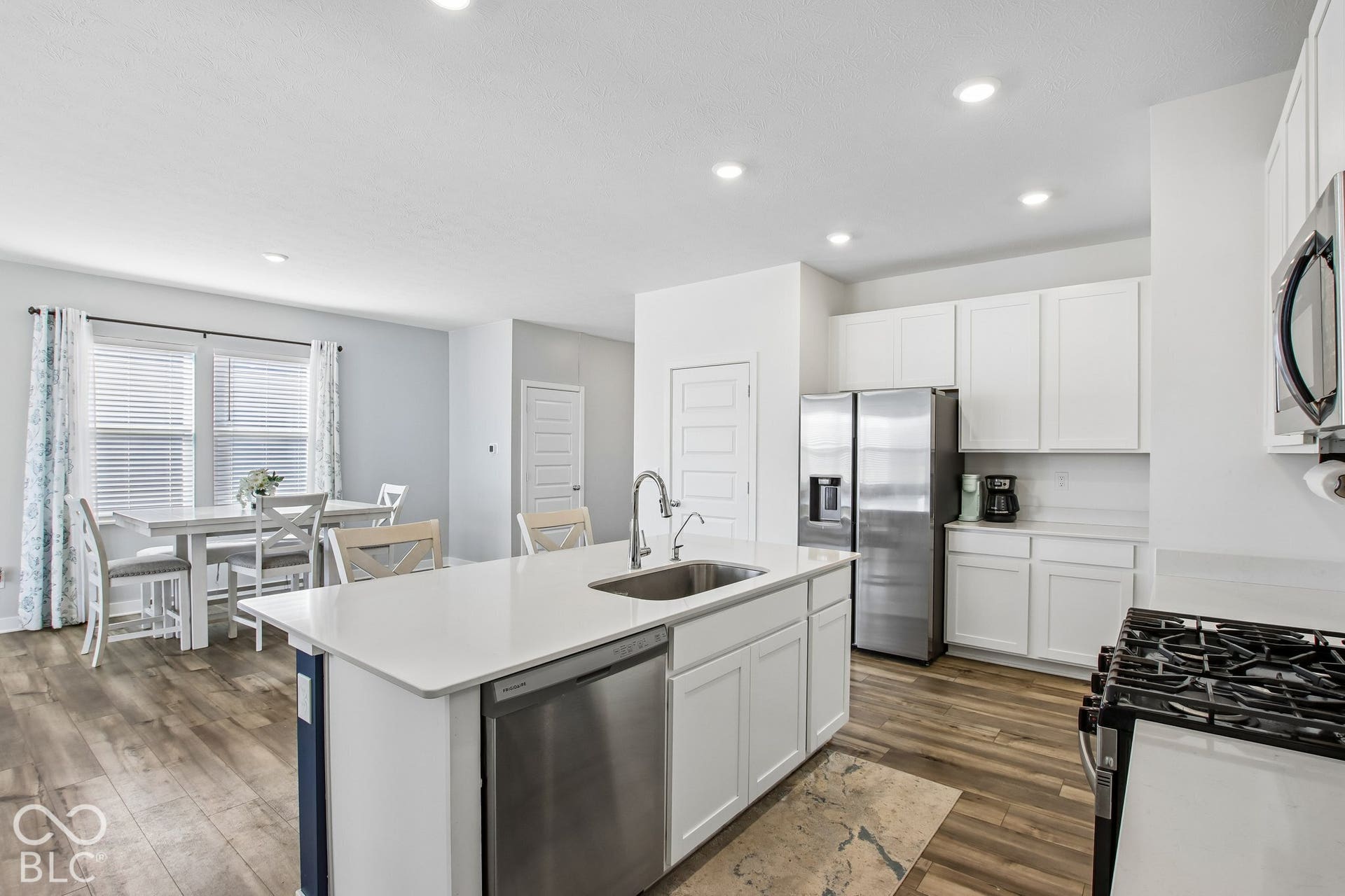 Open-concept kitchen featuring an island with a stainless steel sink, wood-finish flooring, white cabinetry, and stainless steel appliances