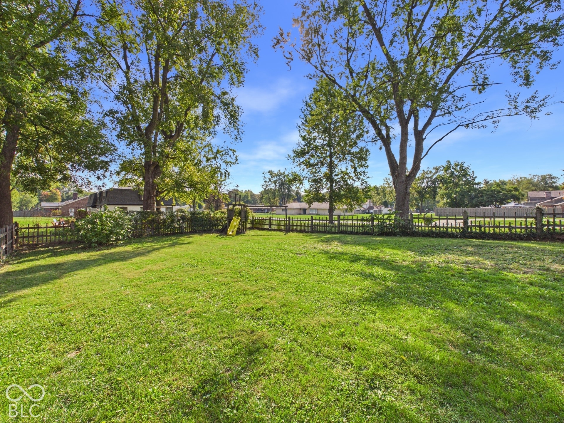 Expansive lawn area featuring mature trees and a wooden picket fence