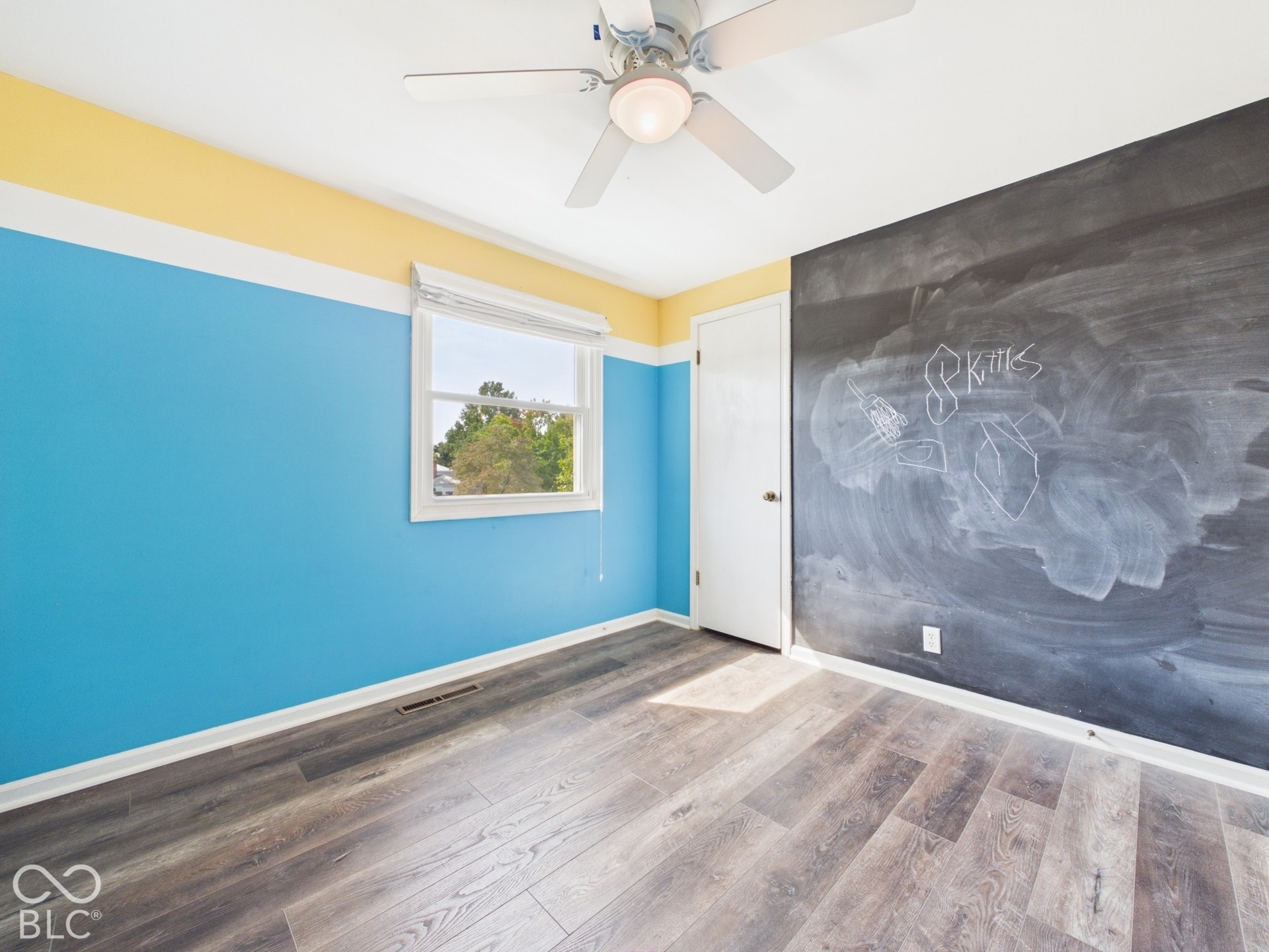 Wood-finish flooring, ceiling fan with integrated lighting, wall-mounted window, and a built-in chalkboard wall feature