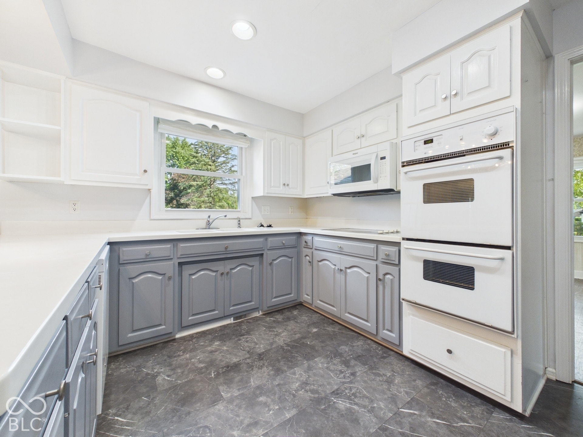 Kitchen featuring two-tone cabinetry, light-toned countertops, a stainless steel sink, built-in double ovens, and recessed lighting