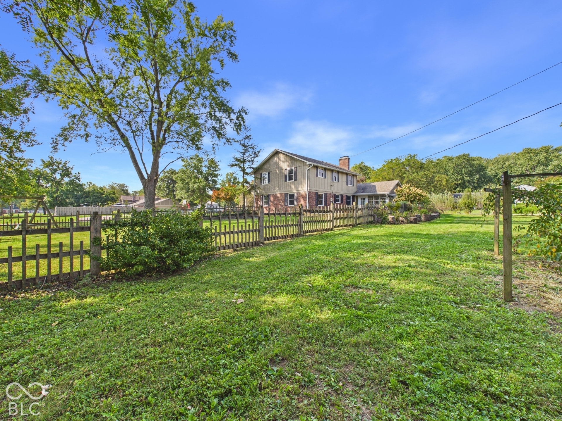 Spacious backyard featuring a manicured lawn, picket fencing, and mature trees