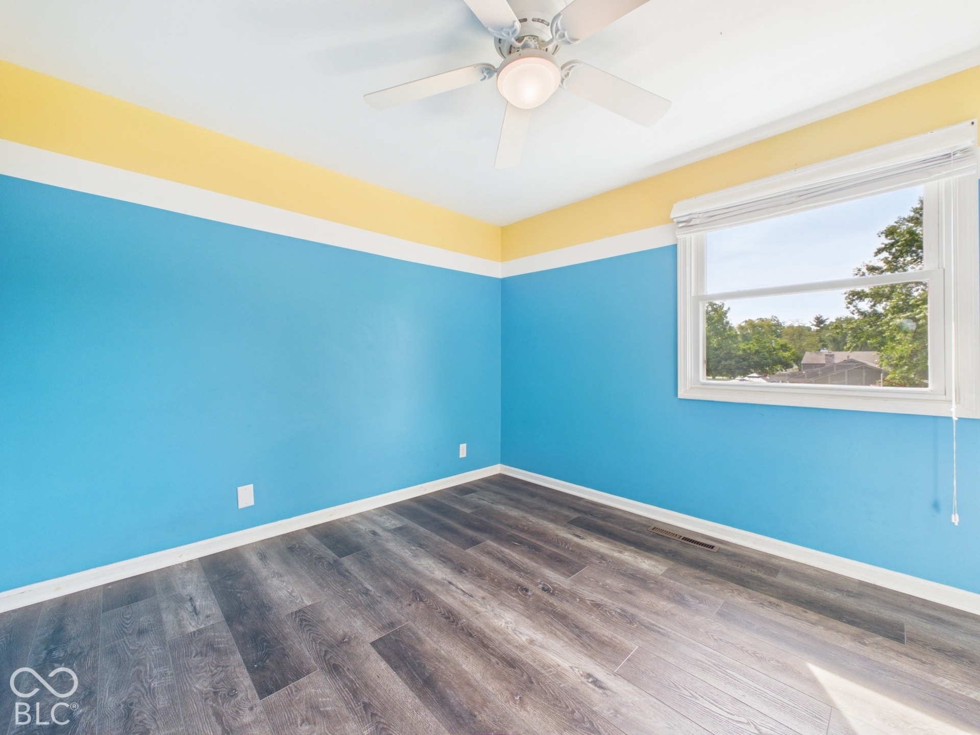 Wood-finish flooring with a ceiling fan light fixture and a single window with blinds