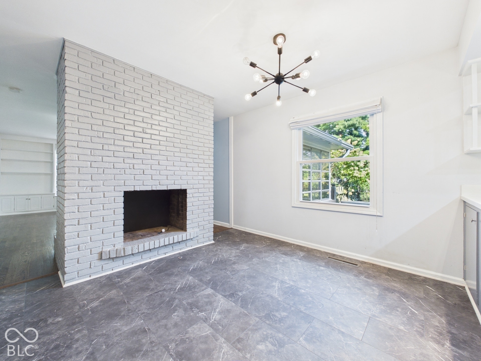 Painted brick fireplace, modern Sputnik-style chandelier, window with grid panes, built-in shelving, and grey wood-finish flooring