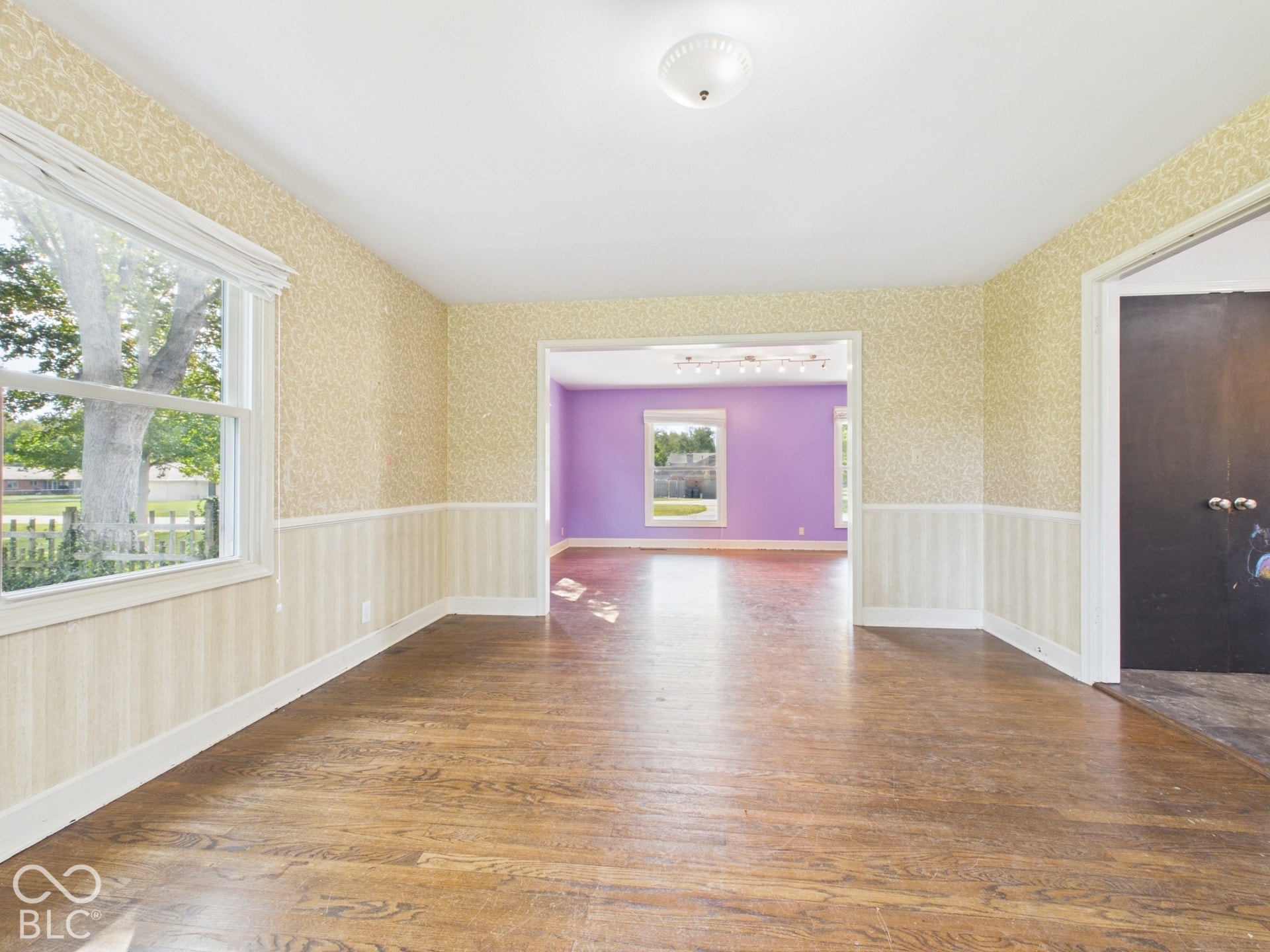 Hardwood flooring throughout, wallpapered walls, white trim, and a window with a white blind