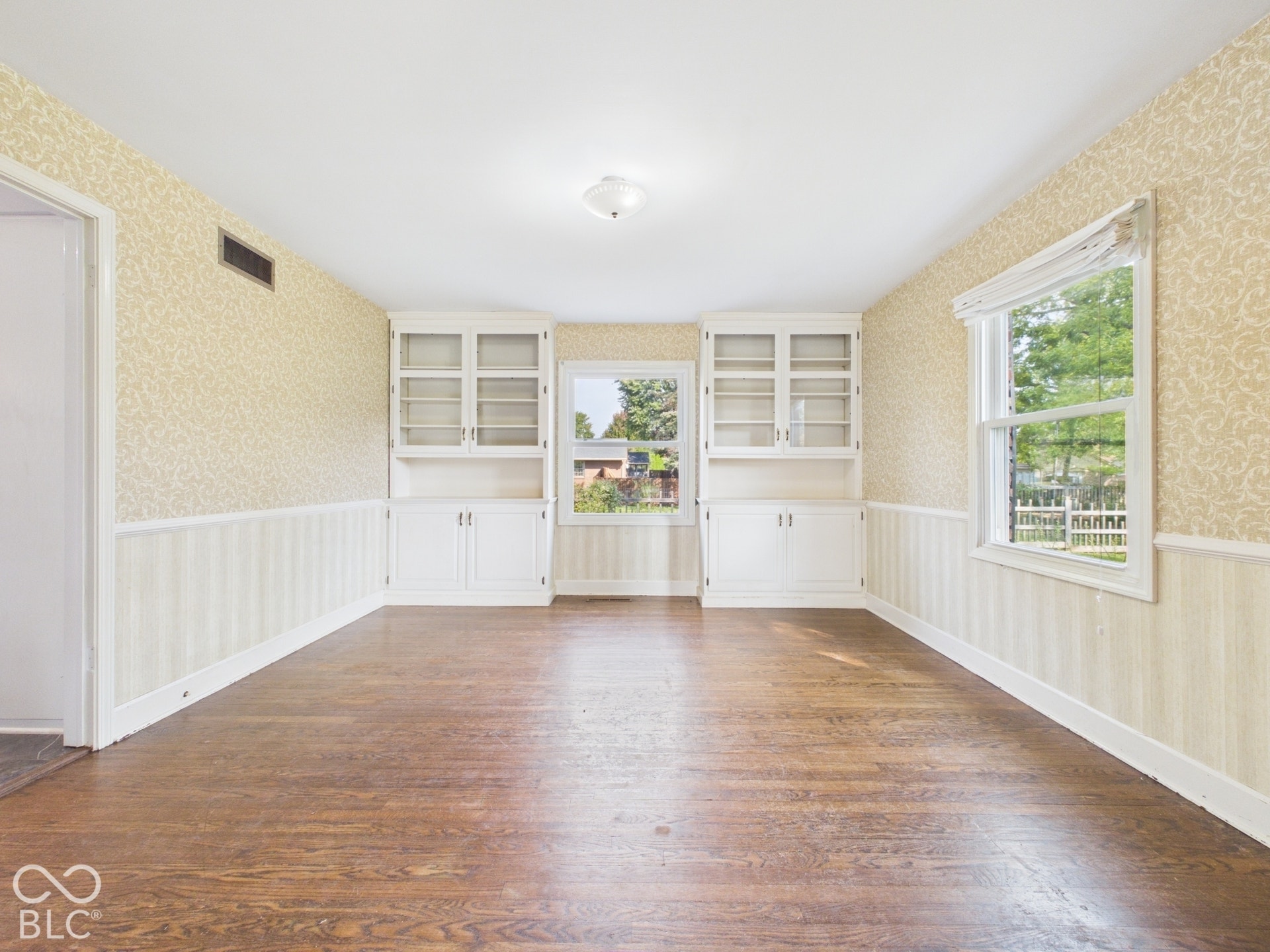 Hardwood flooring, built-in cabinetry with glass-front uppers, two windows, and a ceiling-mounted light fixture