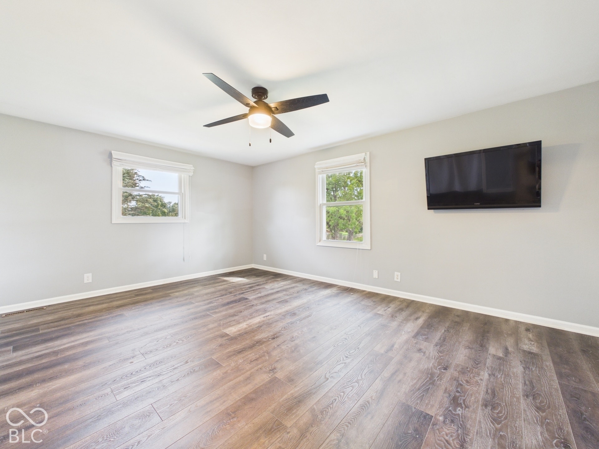 Wood-finish flooring, two windows with blinds, ceiling fan with integrated lighting, and light-toned wall paint