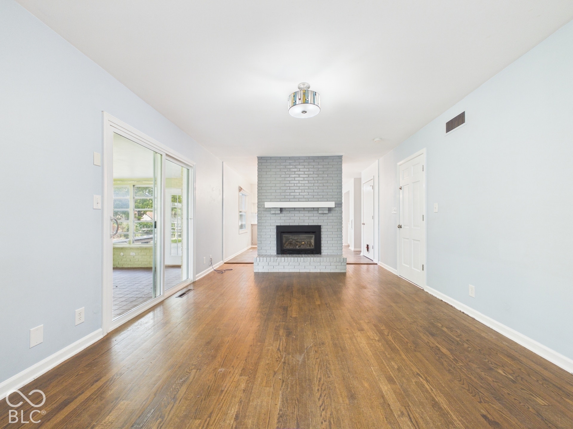 Hardwood flooring, brick fireplace with mantel, recessed fireplace insert, ceiling-mounted light fixture, and sliding glass doors
