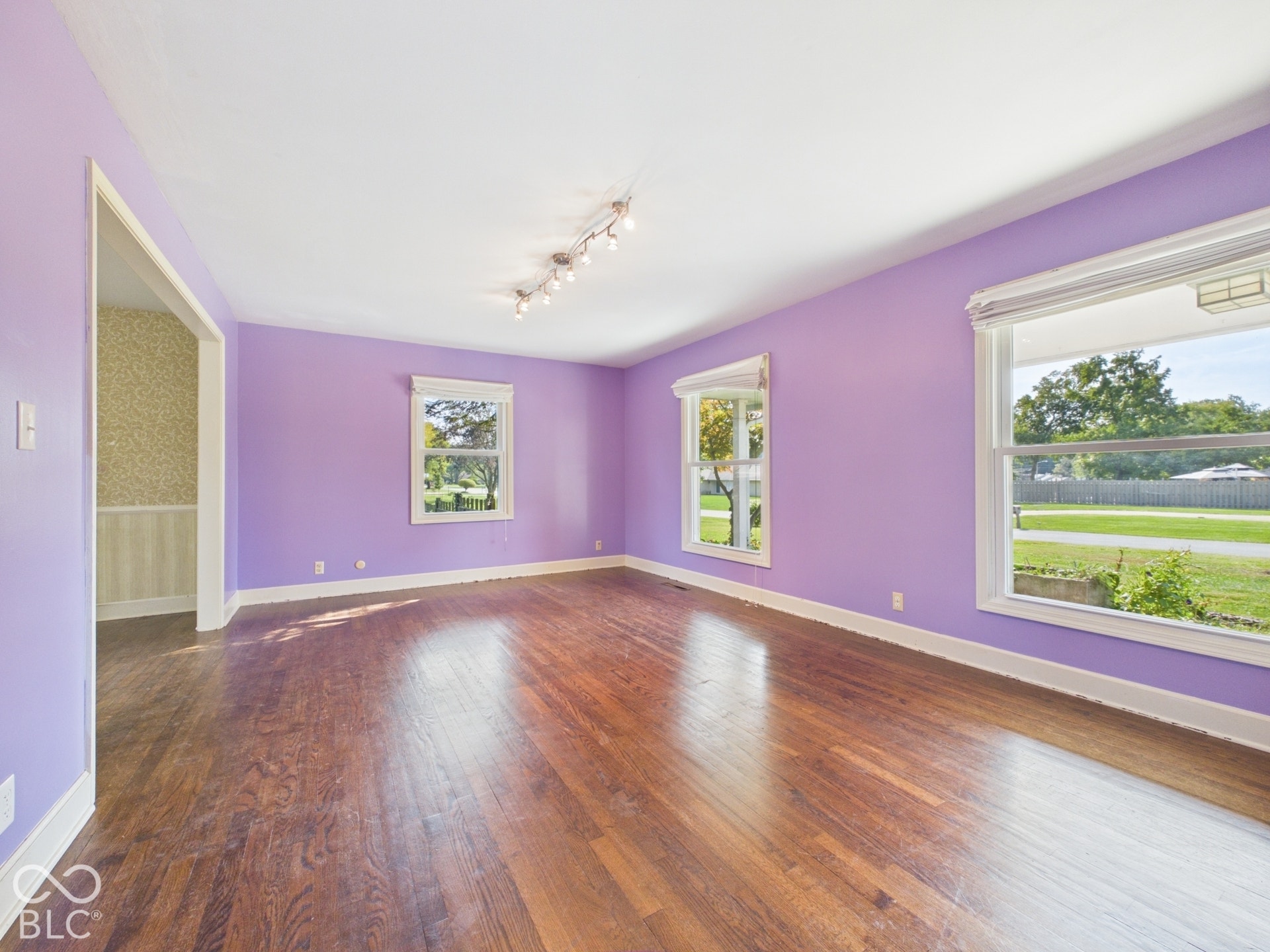 Wood-finish flooring with three windows, white trim, and track lighting