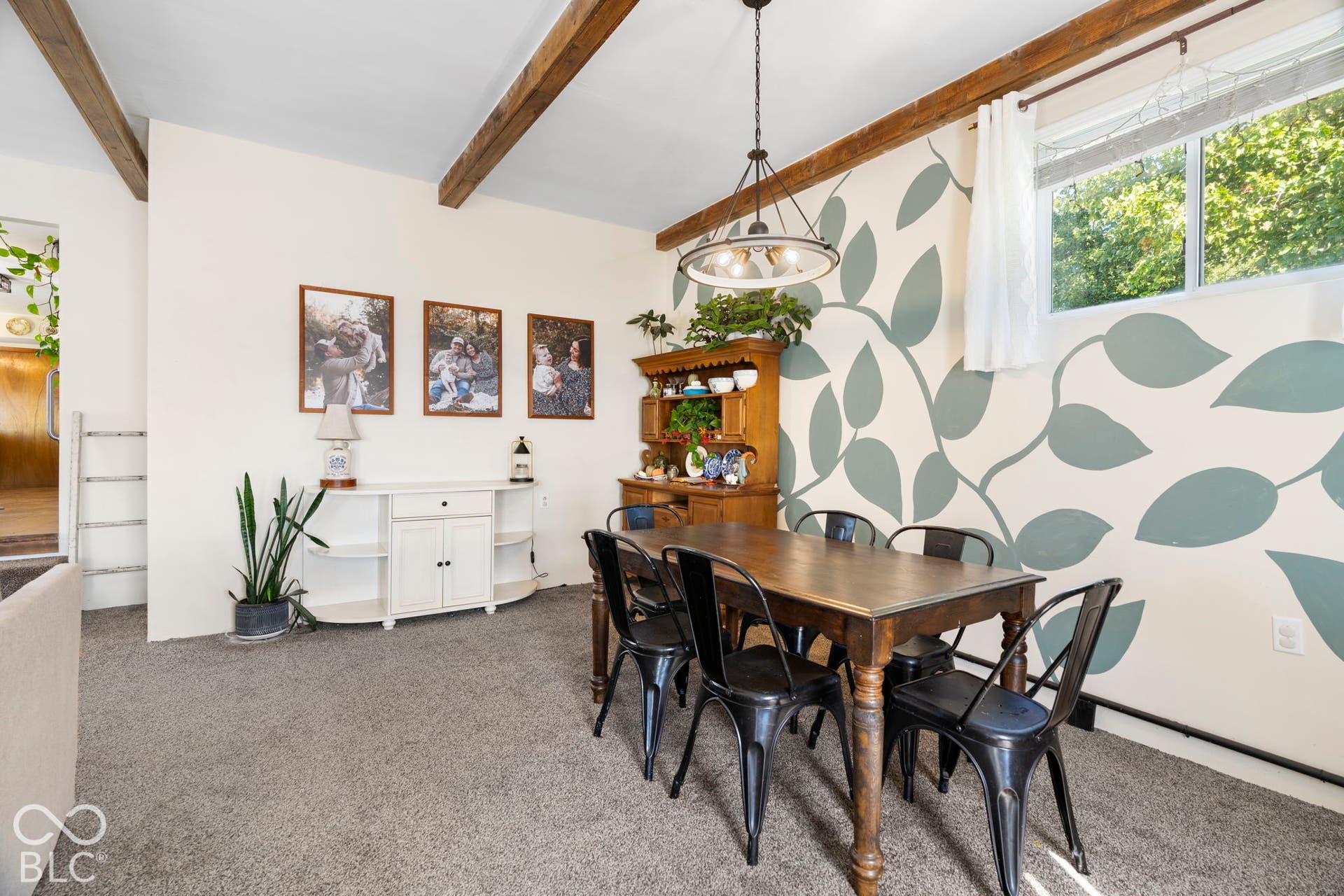 Dining space showcasing exposed wooden ceiling beams, a wood dining table with black chairs, and abundant natural light from large windows