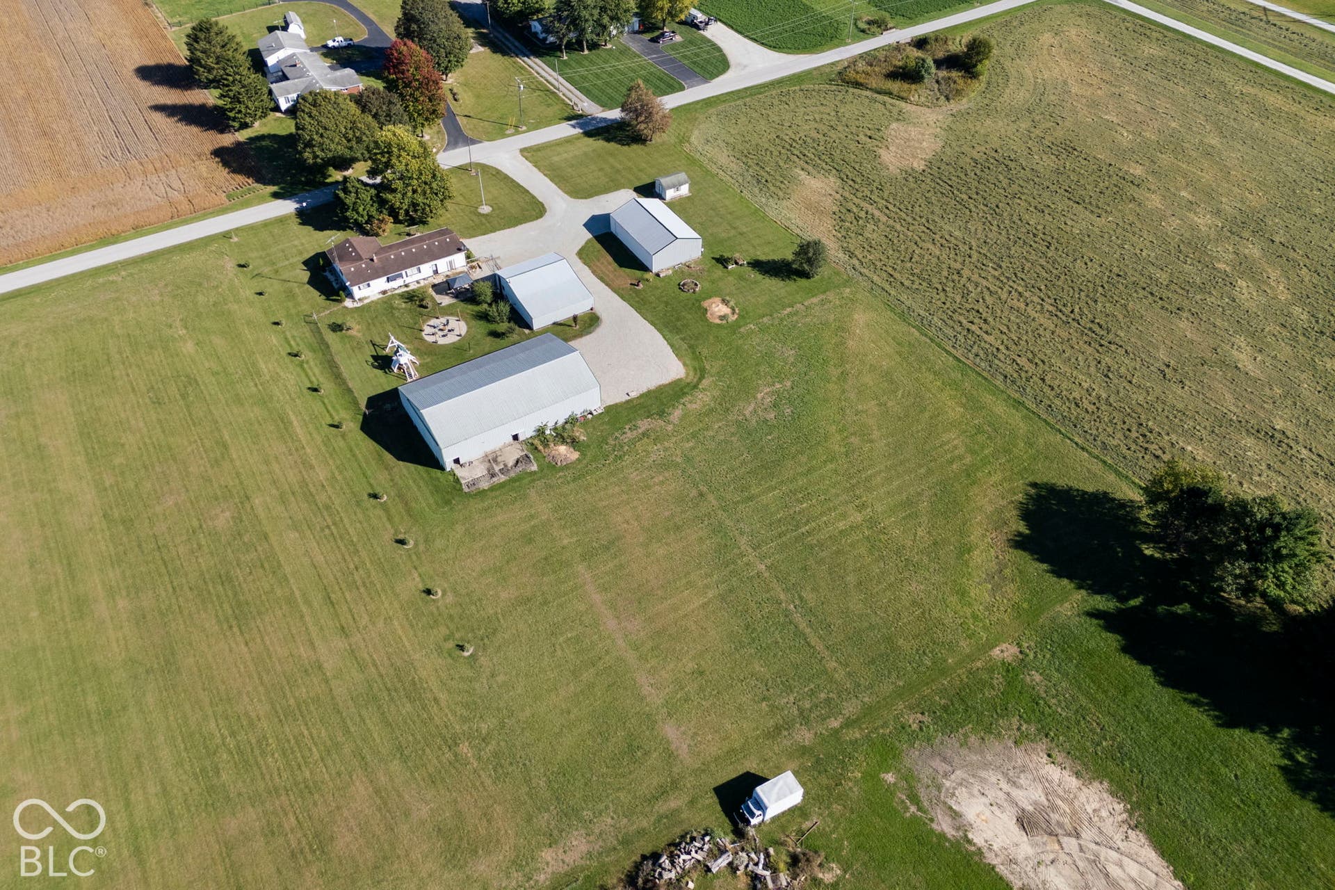 Expansive rural property featuring multiple outbuildings, manicured lawn, mature tree-lined perimeter, and direct road access