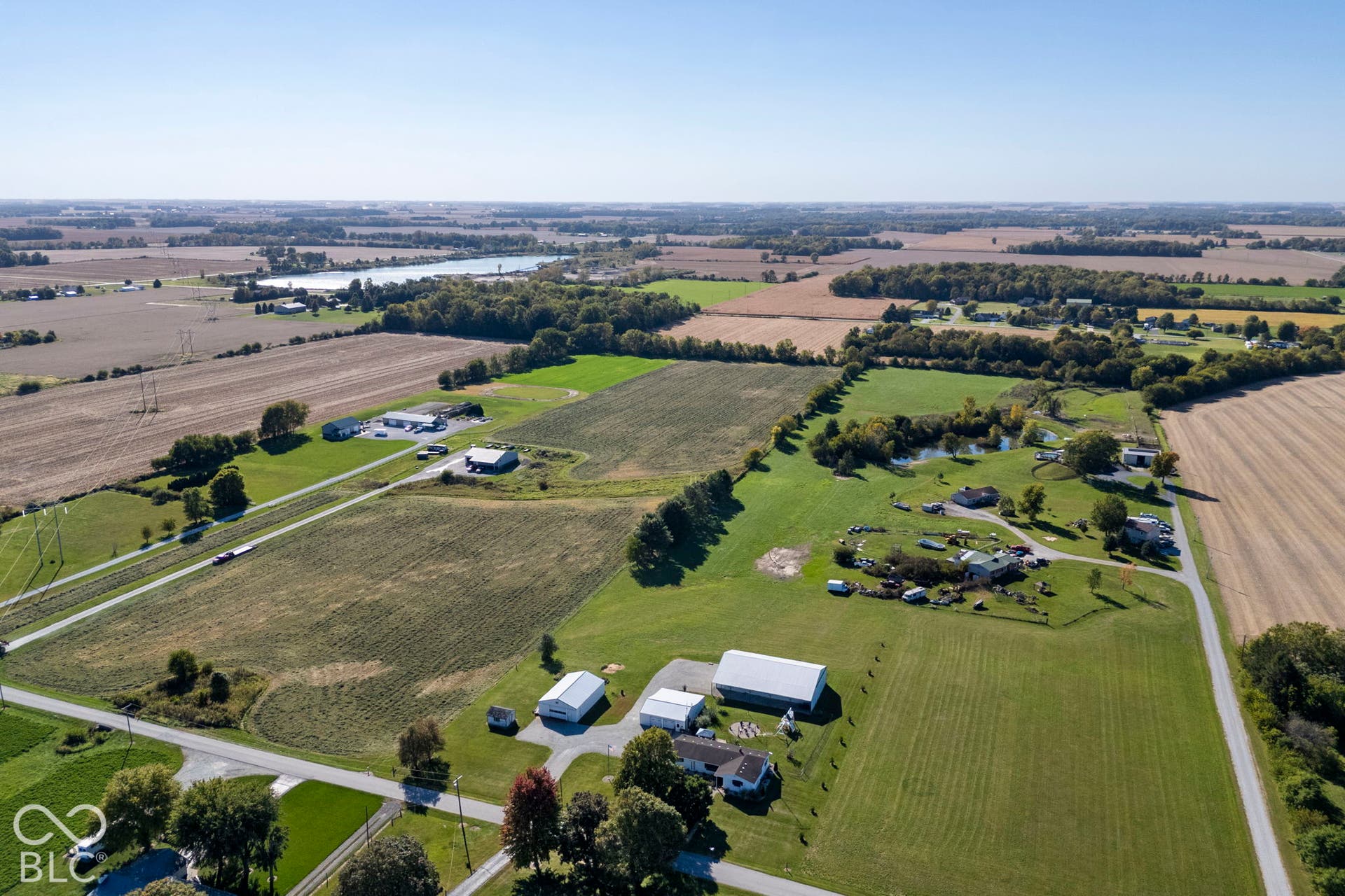 Expansive rural property featuring several structures, a large pond, and multiple fields
