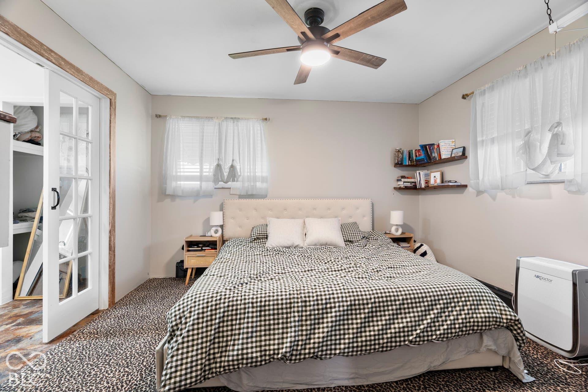 Comfortable bedroom featuring a wood-finish bed frame, carpeted flooring, ceiling fan with integrated lighting, and sheer window treatments