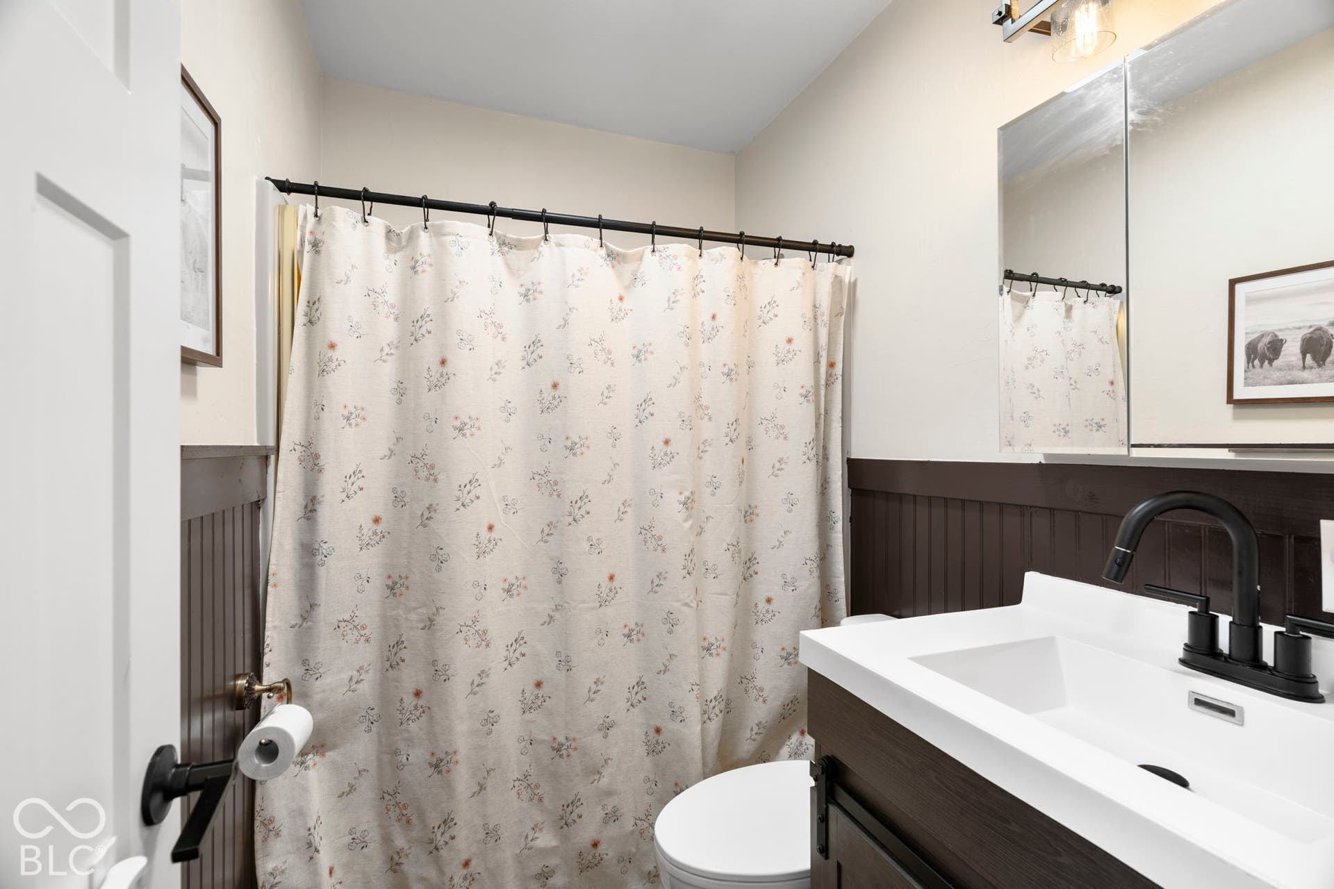 Contemporary bathroom featuring a dark vanity with white countertop and rectangular vessel sink, matte black faucet, large framed mirror, and wainscoting accent wall