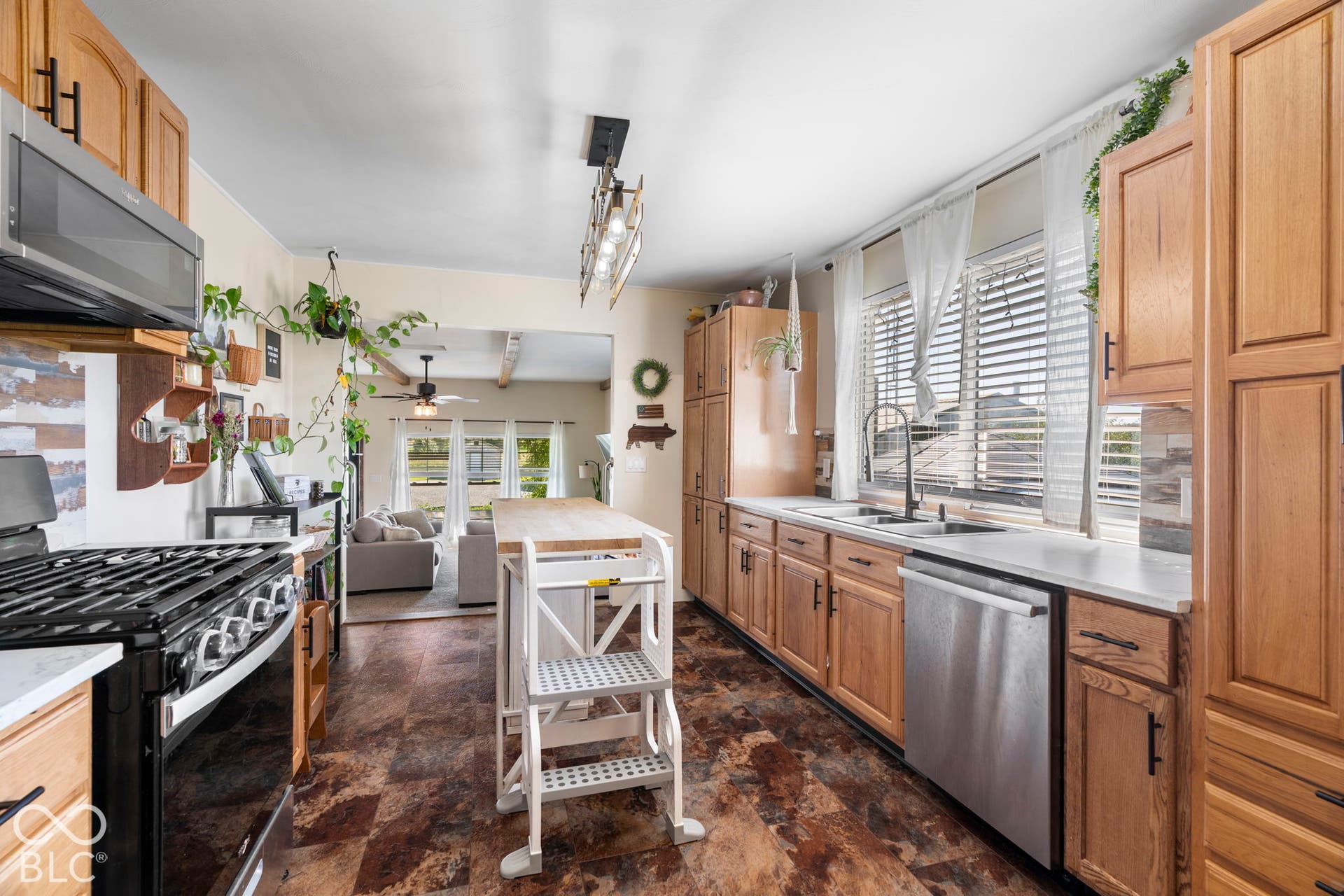 Galley kitchen featuring natural wood cabinetry, stainless steel appliances including a professional-style gas range and dishwasher, granite countertops, and a white island with open shelving