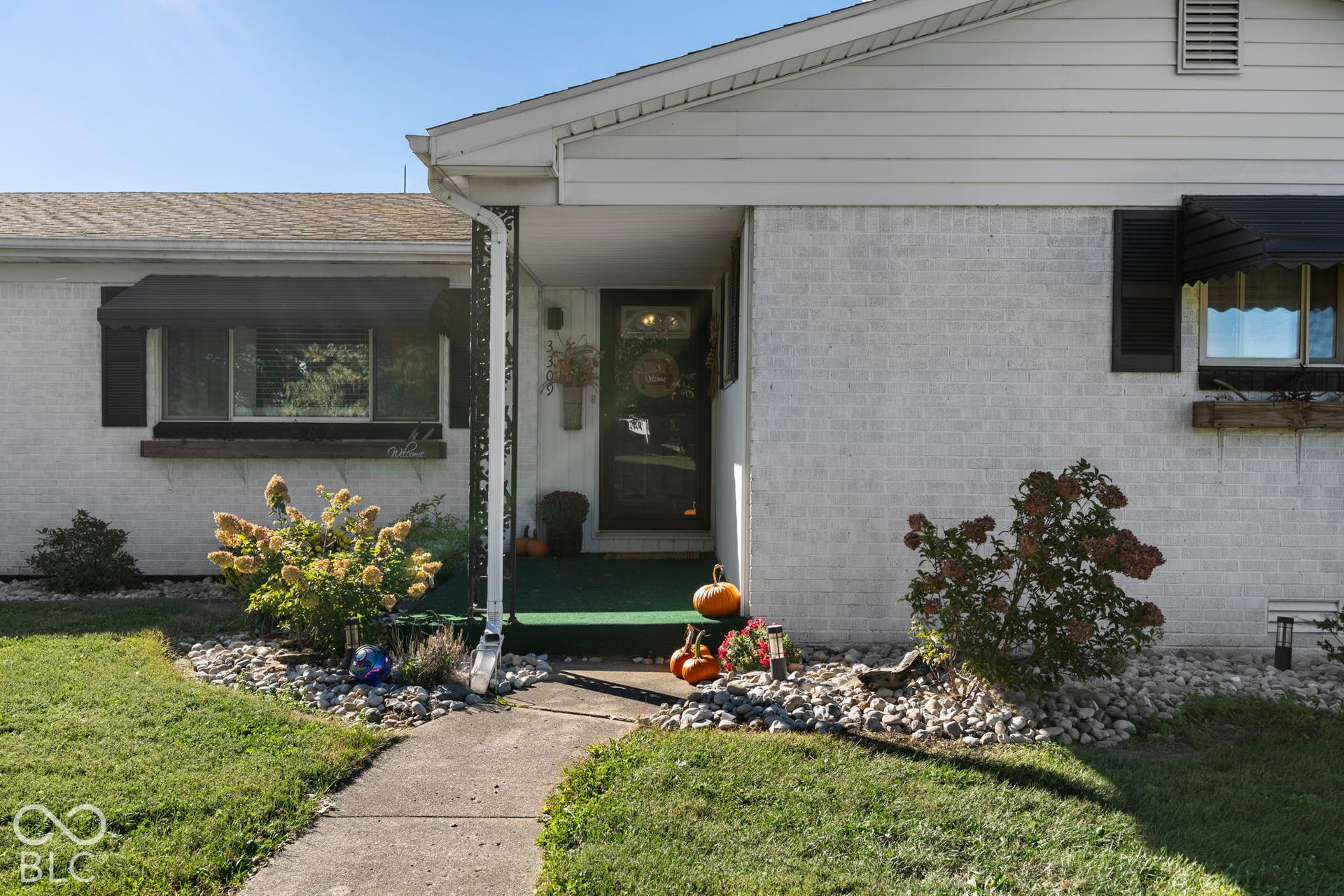 Welcoming front entry with a concrete walkway leading to a covered porch and glass-panel door