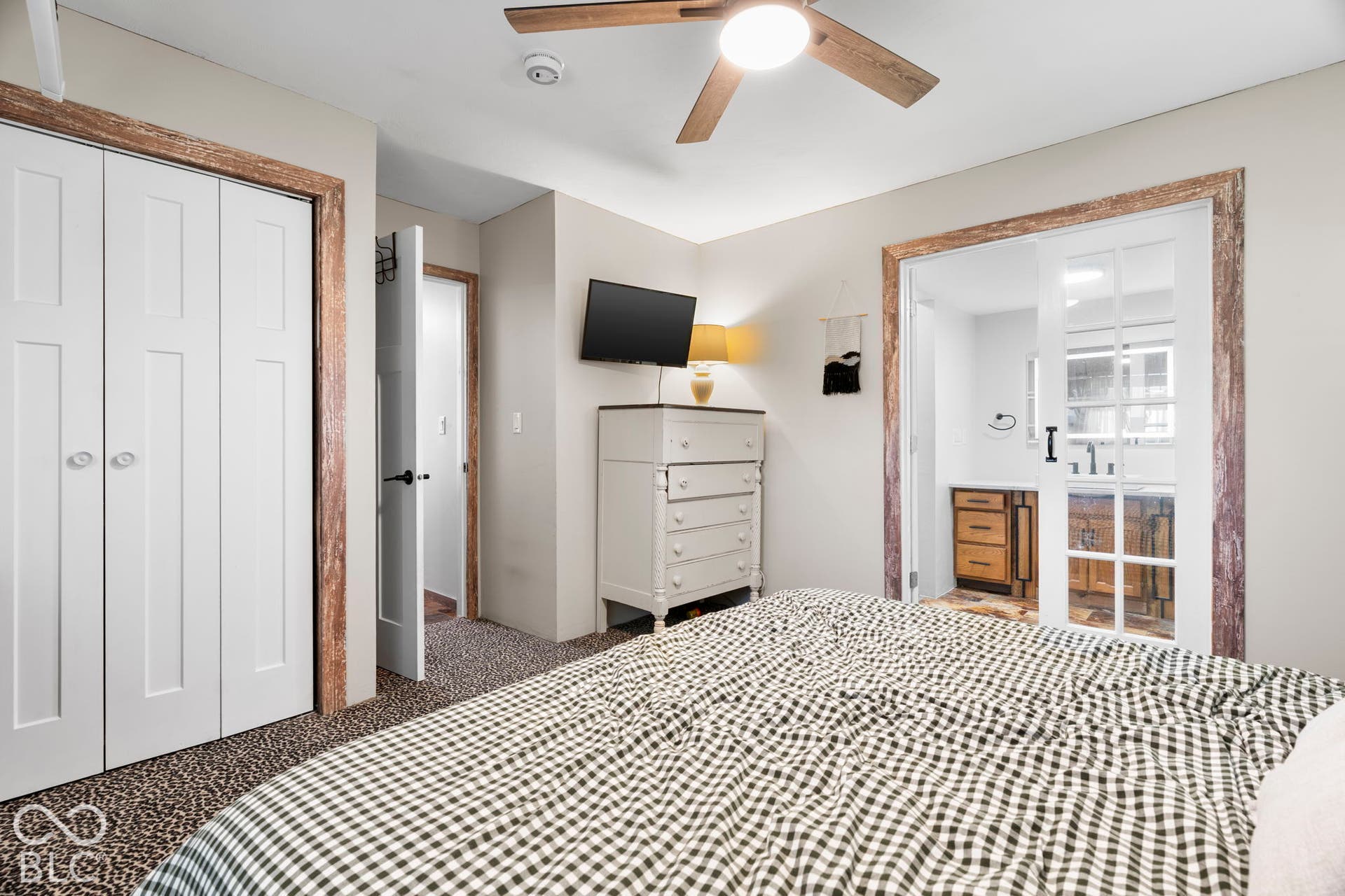 Spacious primary bedroom featuring geometric patterned flooring, ceiling fan with integrated lighting, dual closets with six-panel doors, dresser with drawer storage, wall-mounted television, and abundant natural light from multiple windows