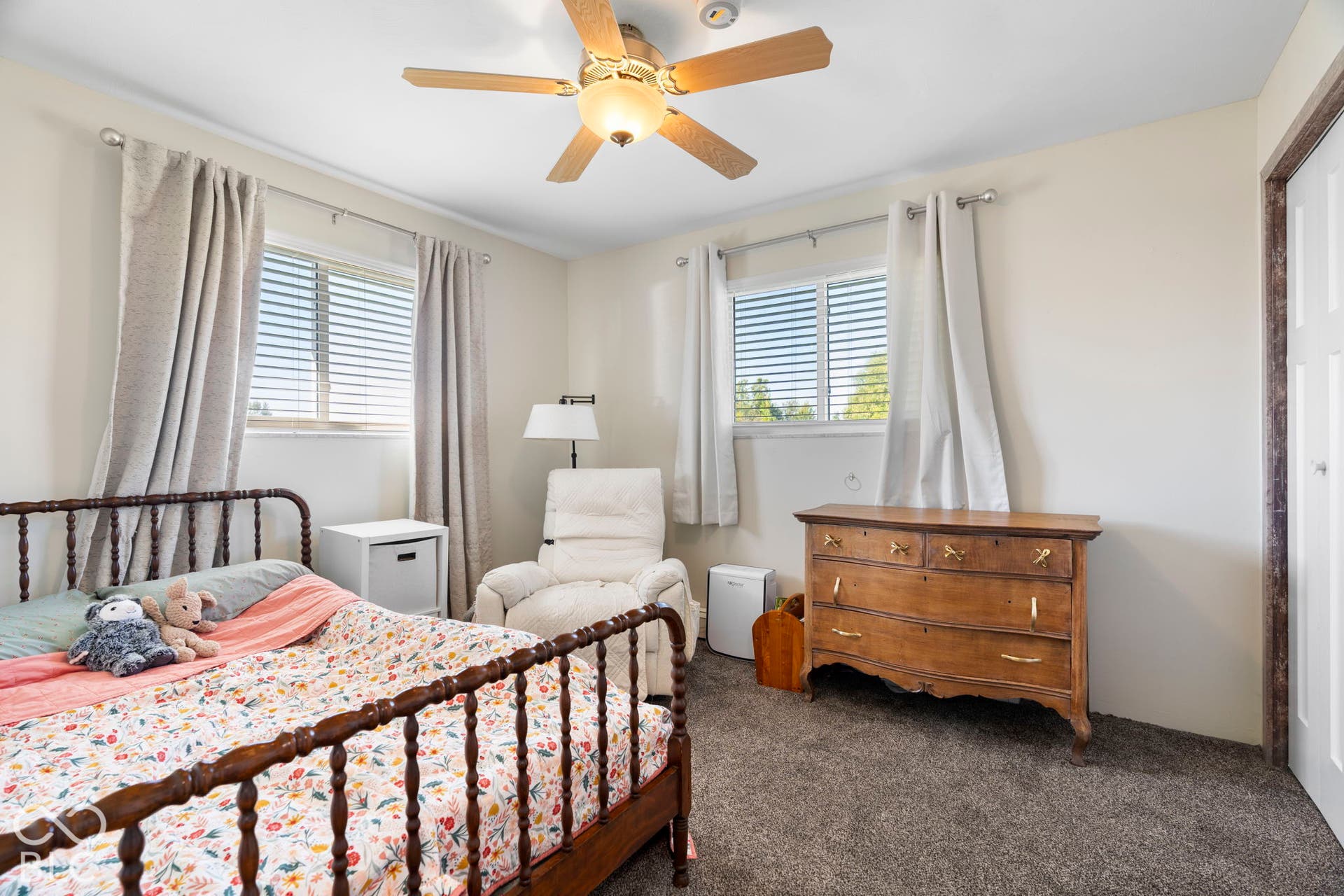 Two windows with horizontal blinds, ceiling fan with integrated lighting, textured carpeting, and a white interior door