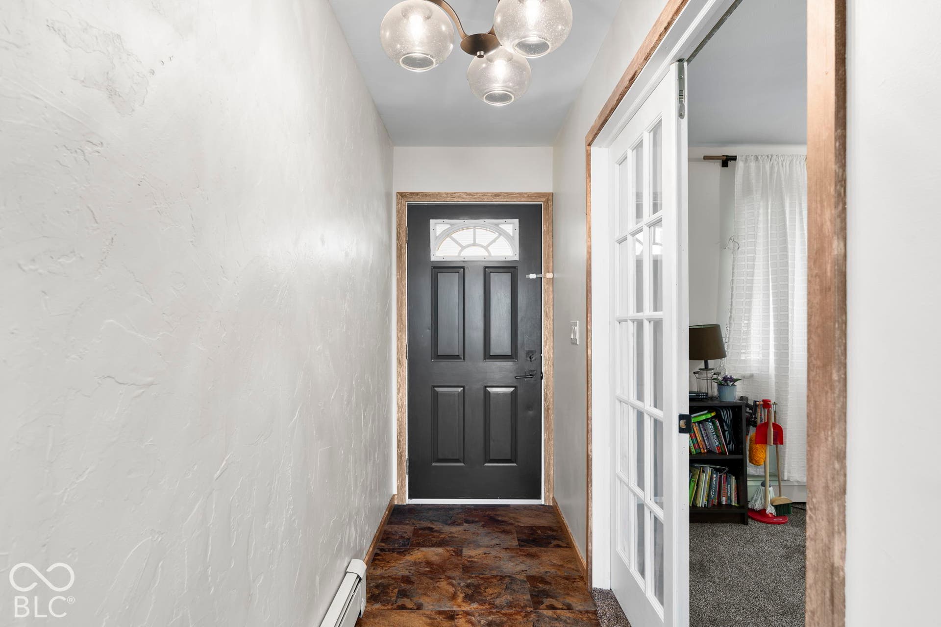 Welcoming foyer featuring a dark six-panel entry door with transom window, polished pendant lighting, textured white walls, and rich wood-finish flooring that extends throughout the entry corridor