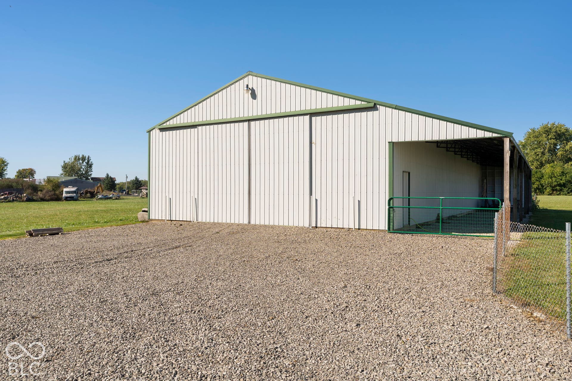 Spacious metal-frame agricultural building featuring a gabled roof design, gravel apron, and wide open-air entry bay