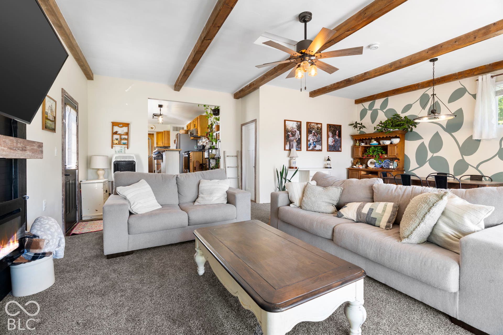 Spacious living area showcasing exposed wood beam ceiling details, ceiling fan with integrated lighting, and neutral upholstered seating arrangements